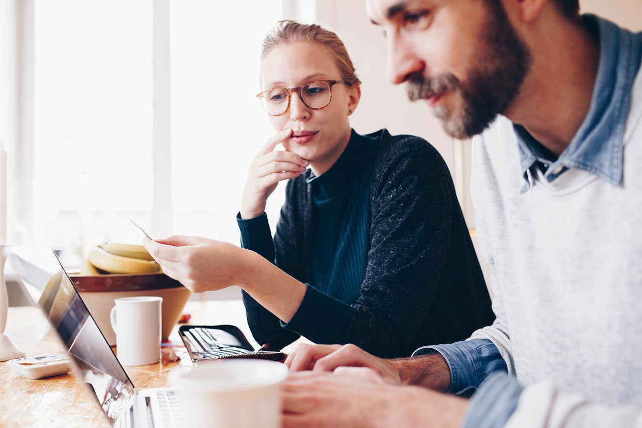 Man and woman sitting at a table looking at a laptop screen together 