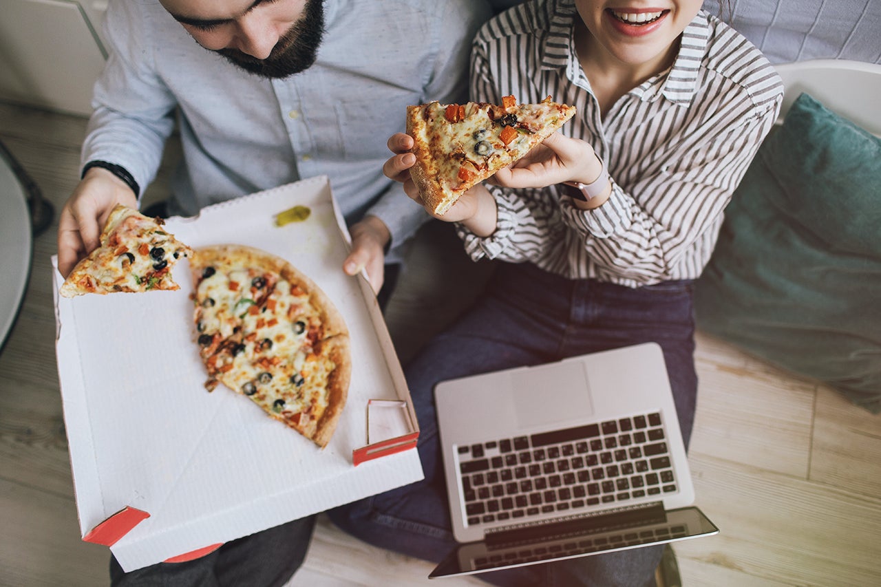 overhead view of a young couple eating pizza and watching movie on laptop together