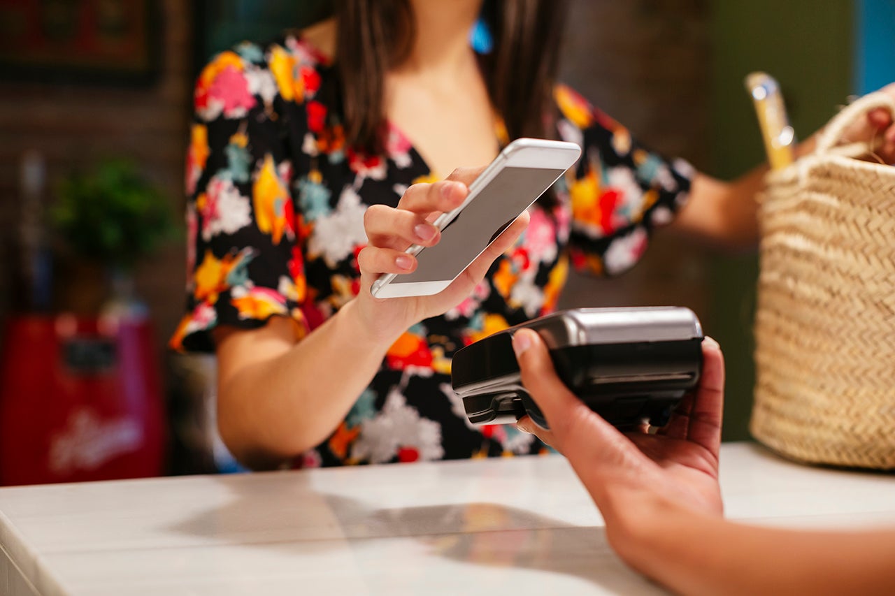 an unseen person holds their smart phone over a credit card machine to make a mobile wallet payment