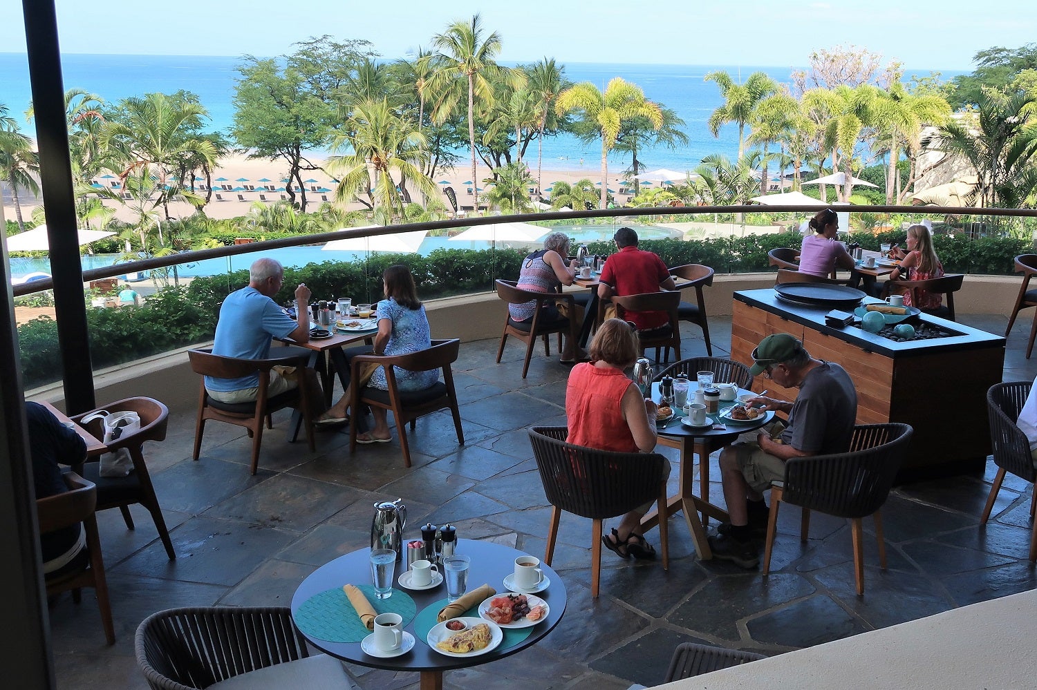 people eat at a restaurant deck overlooking palm trees and a beach