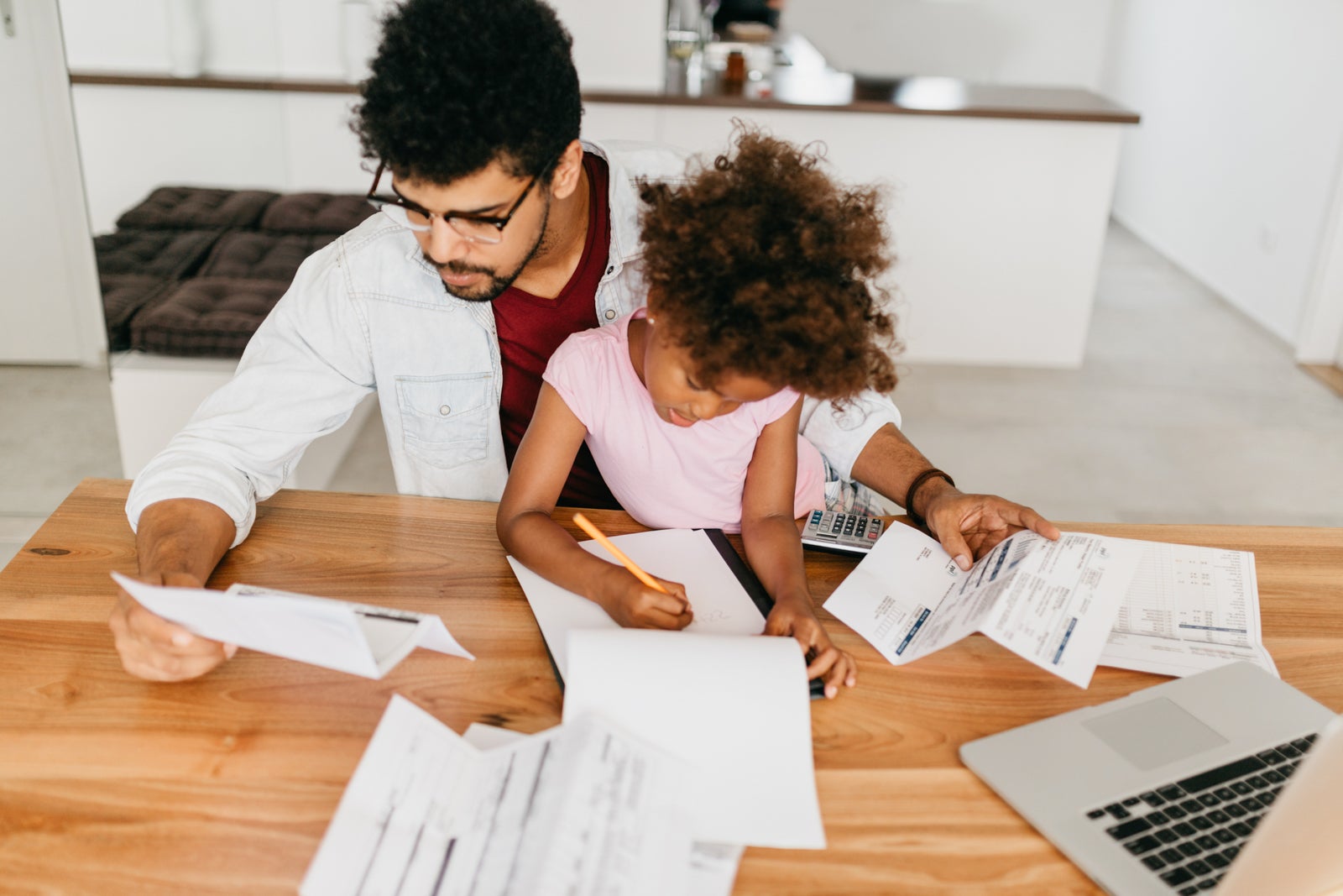 a father and young daughter look at bills on a dining room table