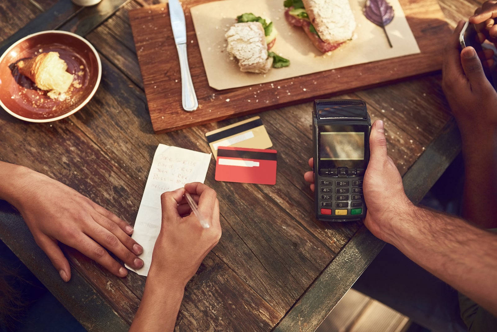 an unseen person signs a receipt after paying for a meal with a credit card