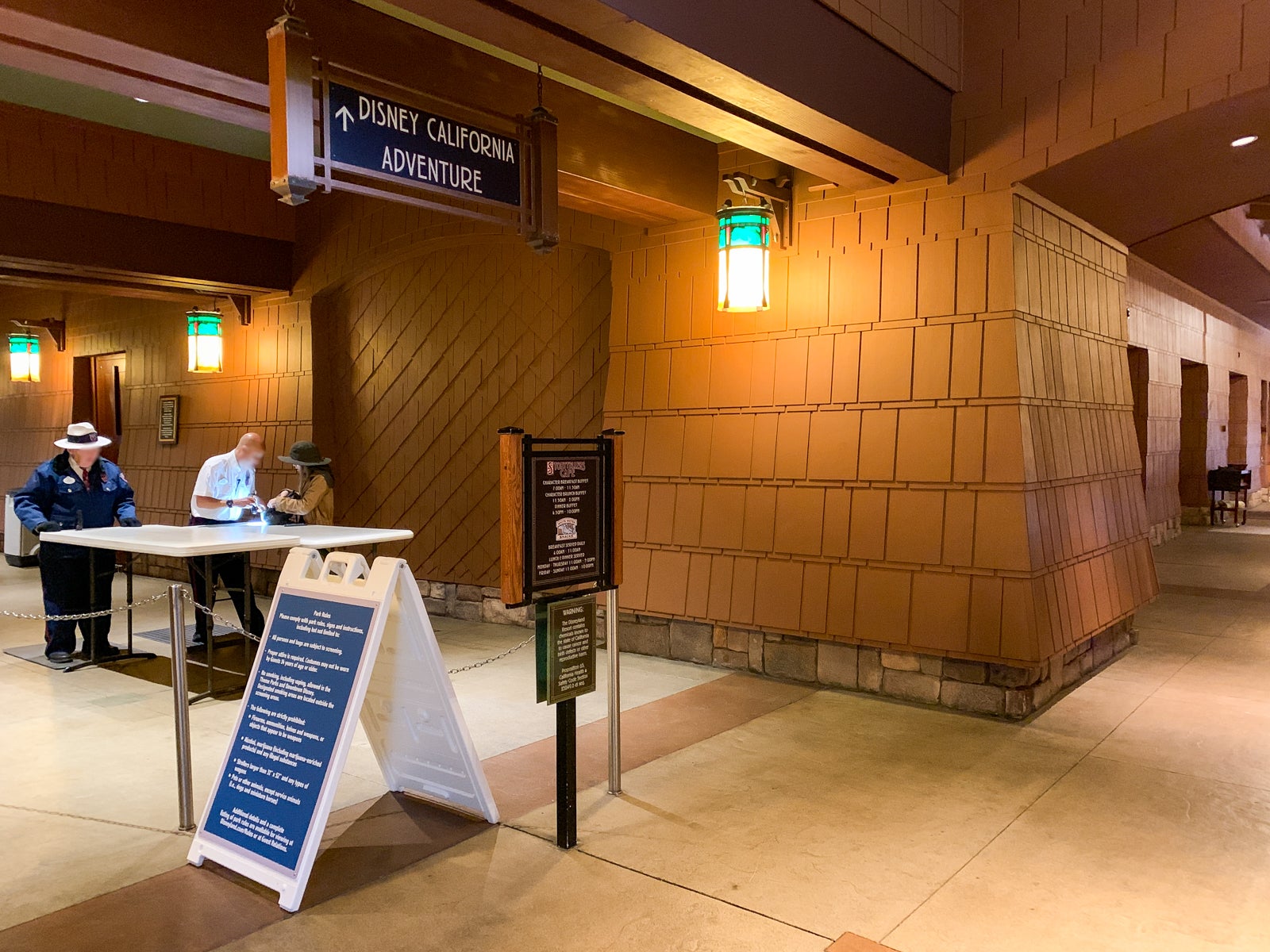 security guards check a bag at a table in a hallway, with a sign above pointing to Disney California Adventure
