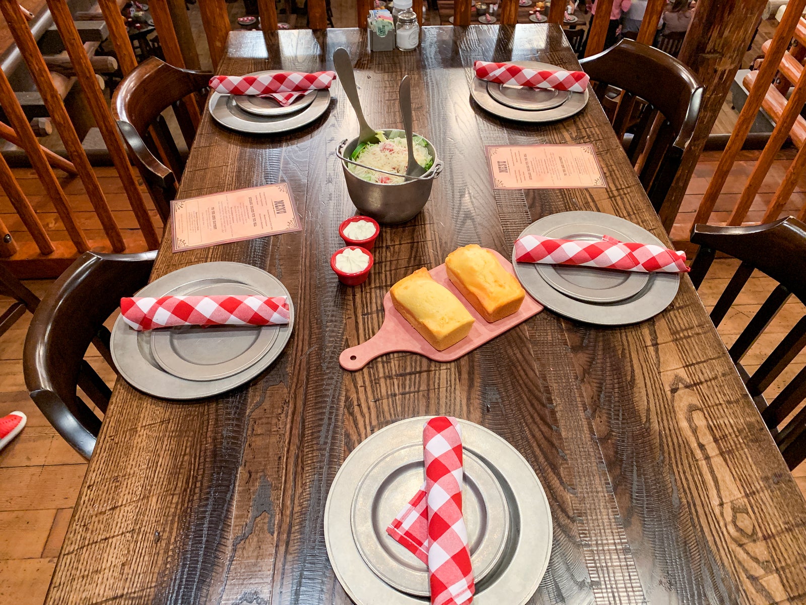 An empty table is set with metal plates, red and white checked napkins, cornbread and a bowl of salad at Hoop-Dee-Doo Revue at Disney's Fort Wilderness Resort