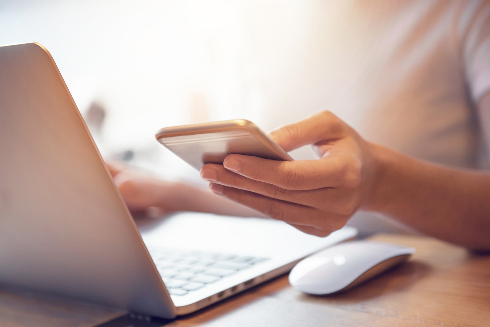 Person holding their smartphone while using a laptop