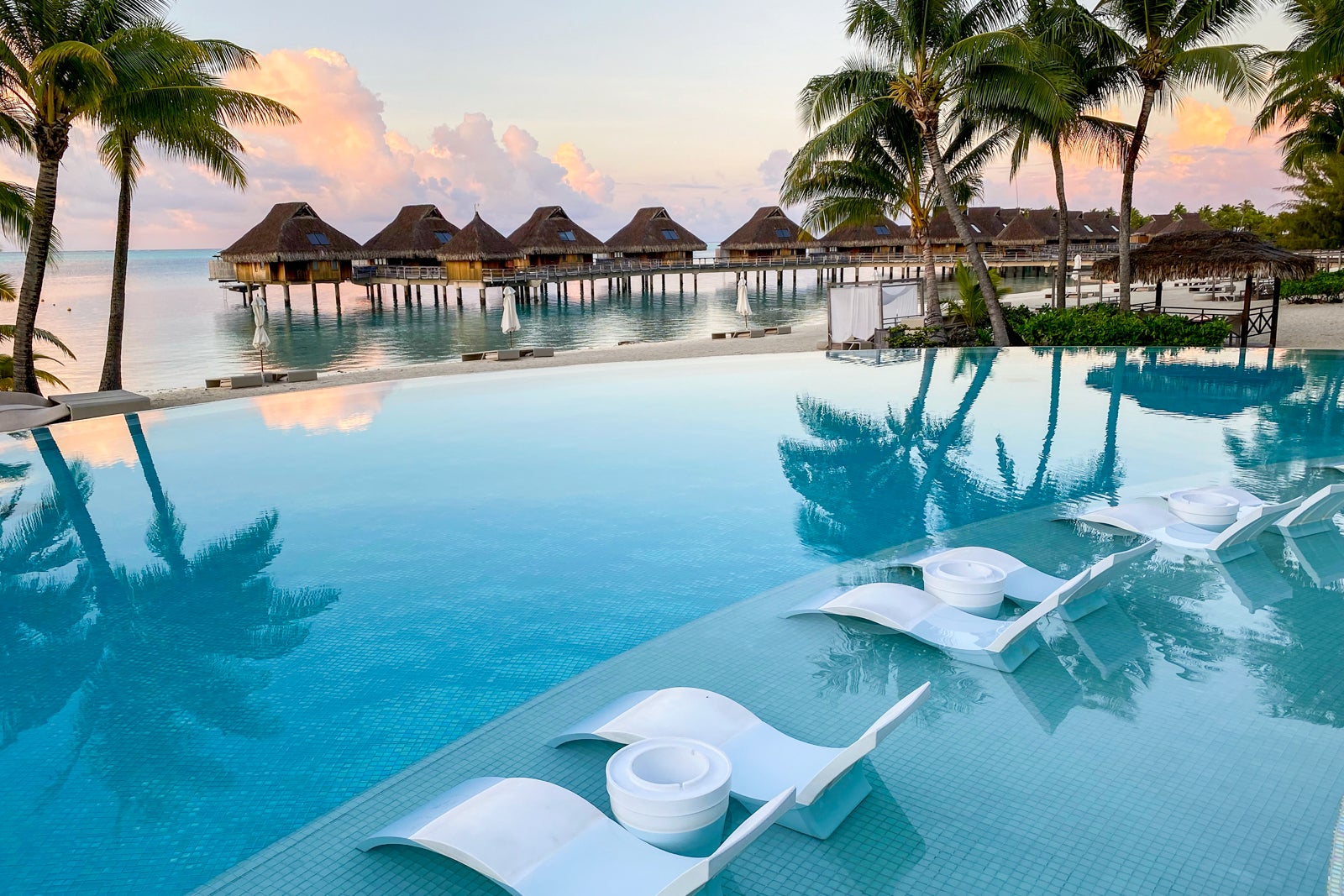an infinity pool in the foreground with overwater bungalows in the background, all at a luxury resort