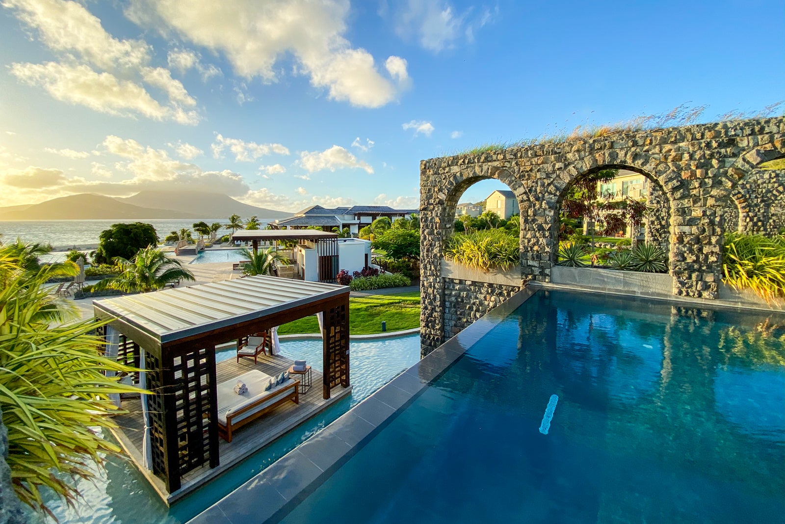 looking from a second-story infinity pool over pool cabanas toward the ocean, all seen at a luxury hotel