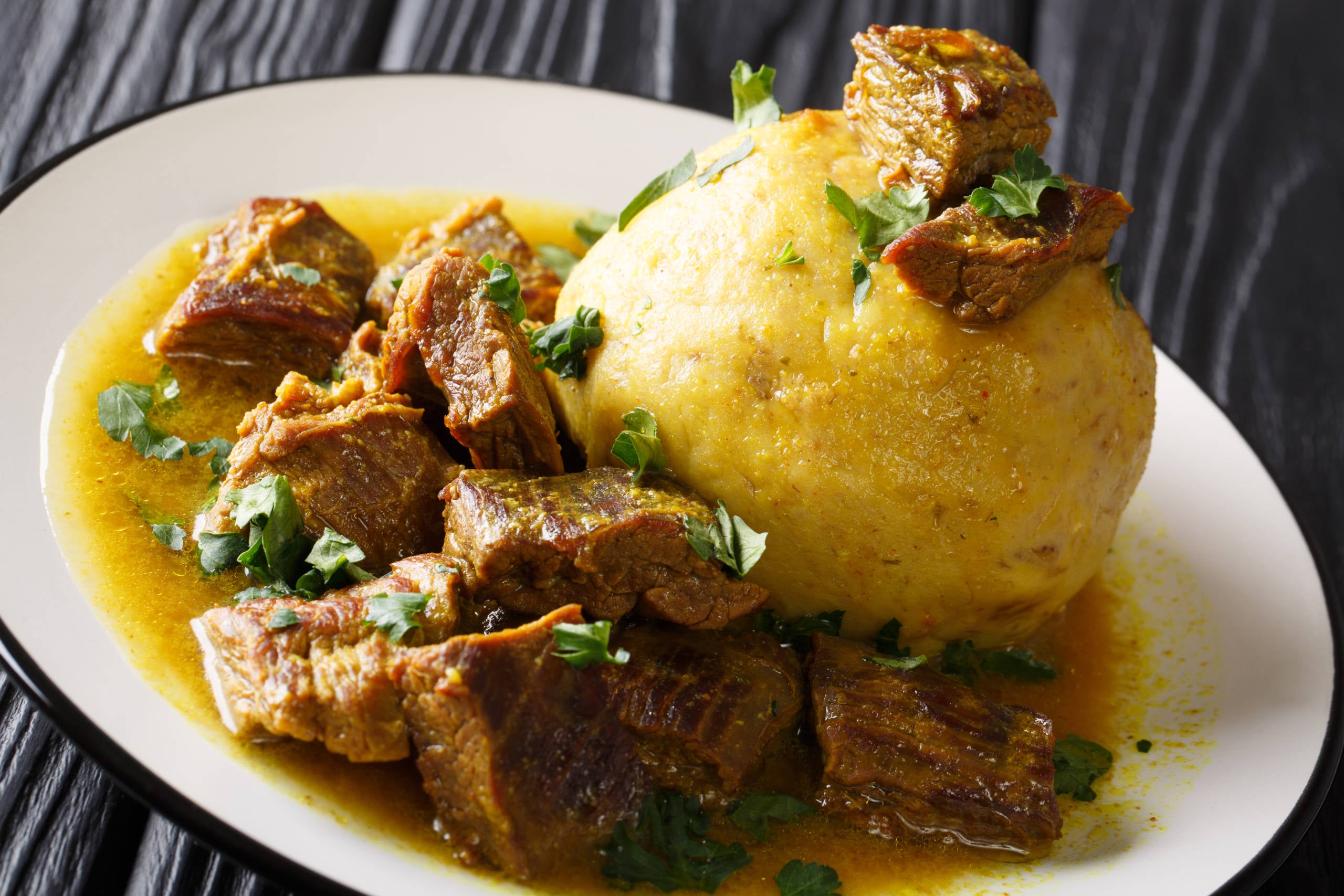 Puerto Rican Mofongo made from plantains, garlic and chicharron served with meat and broth close-up on a plate on the table. horizontal