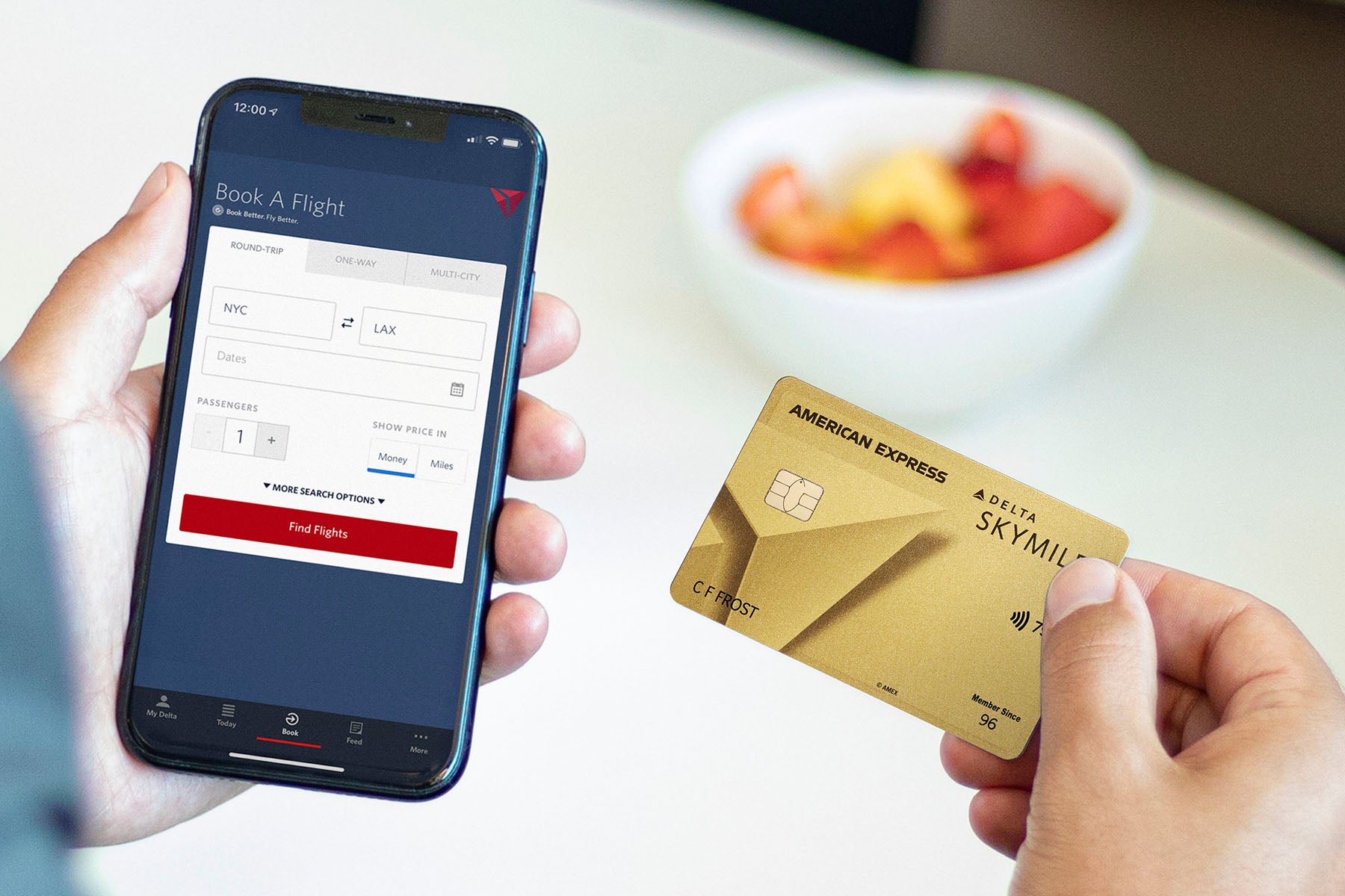 a hand holds the Delta Gold card from Amex while using the Delta app on a phone