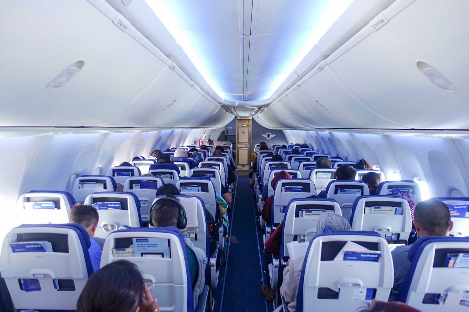 looking from the back of the plane up the center aisle toward the front of a plane, full of passengers