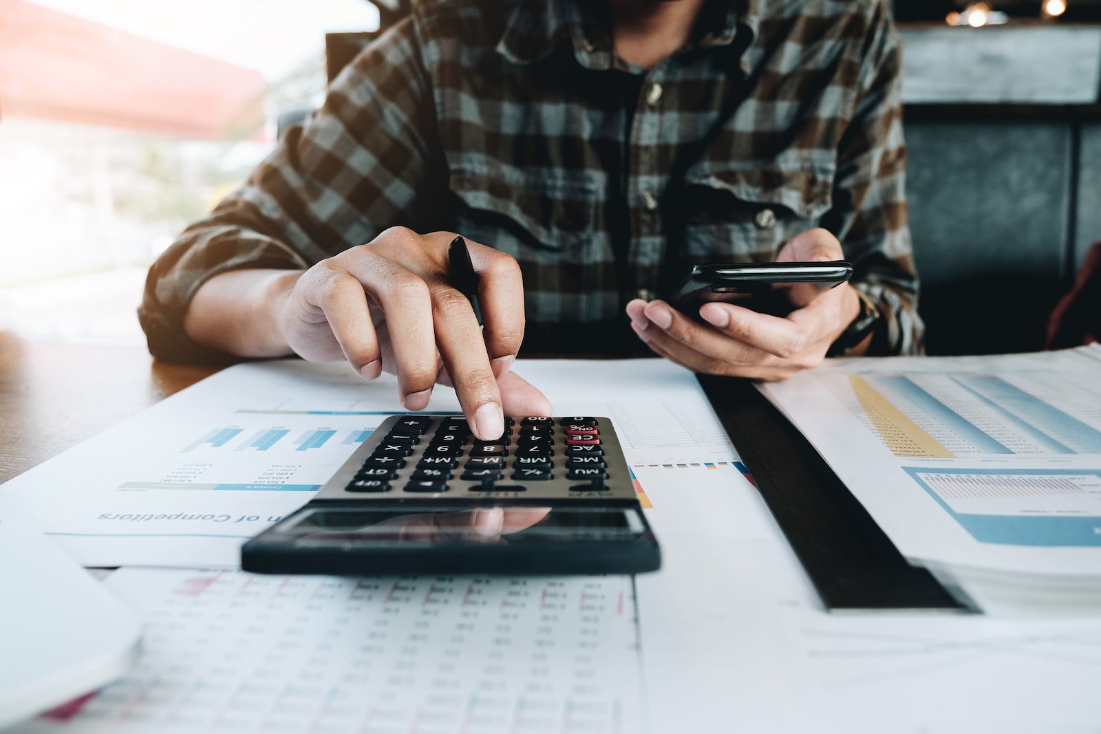 an unseen person uses a calculator while preparing tax documents