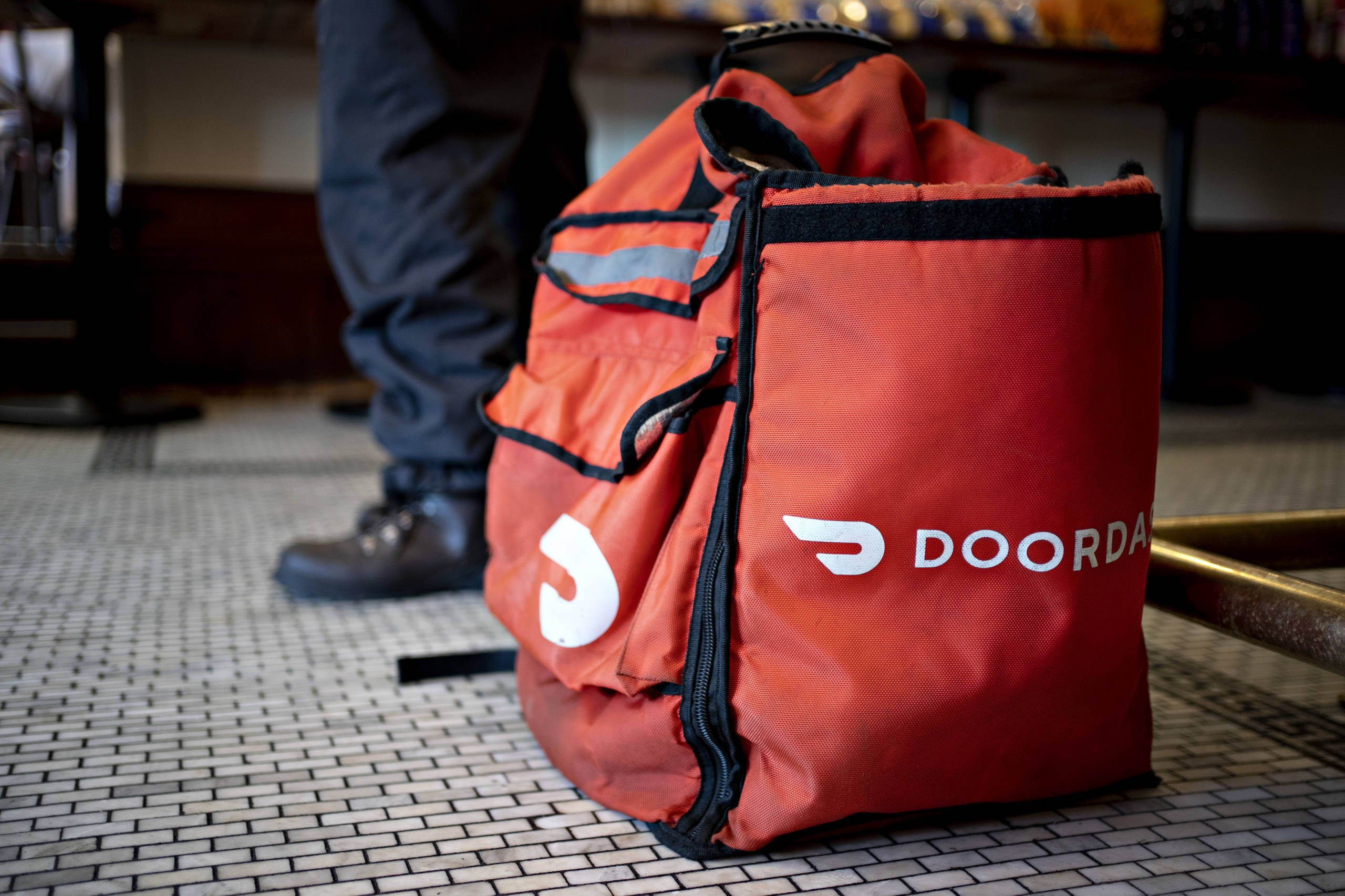 a DoorDash food delivery bag sits on the floor near an unseen person's feet