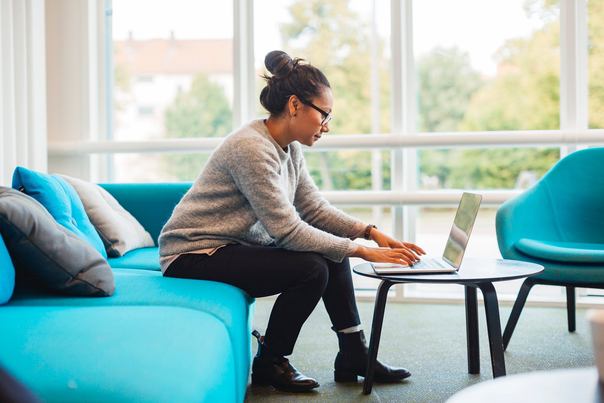 woman sits on couch while using laptop