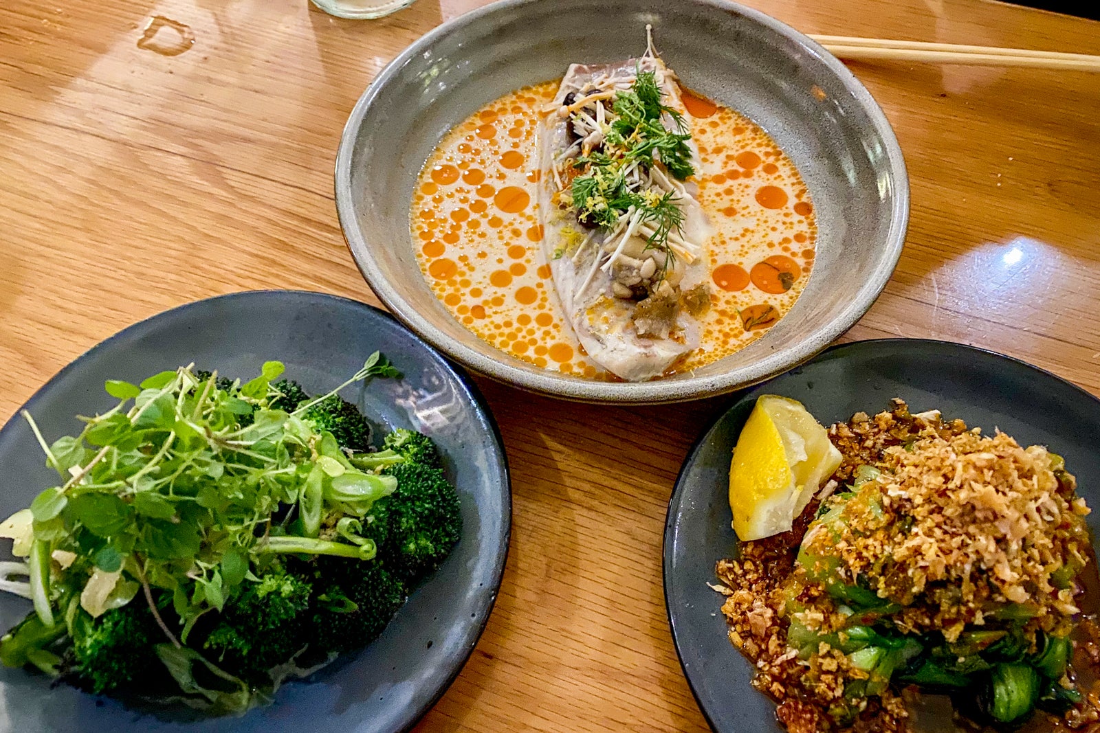 three plates of fish, salad, and grains on a table