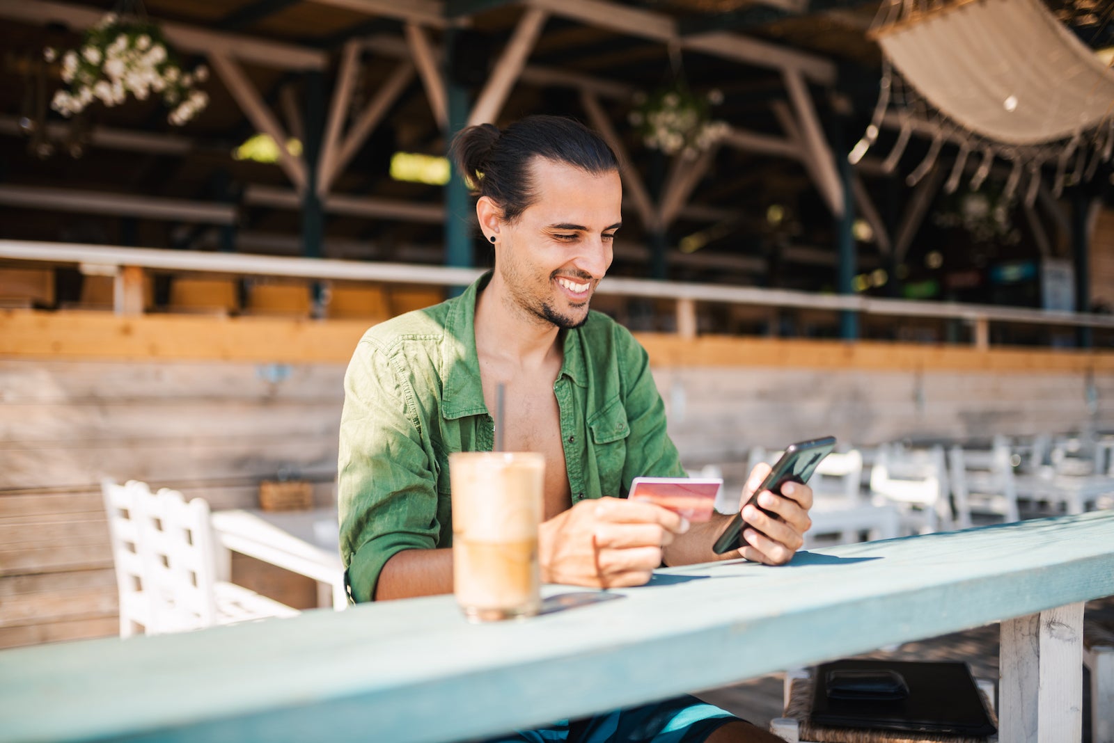 a young man sits at a cafe while shopping on his smartphone