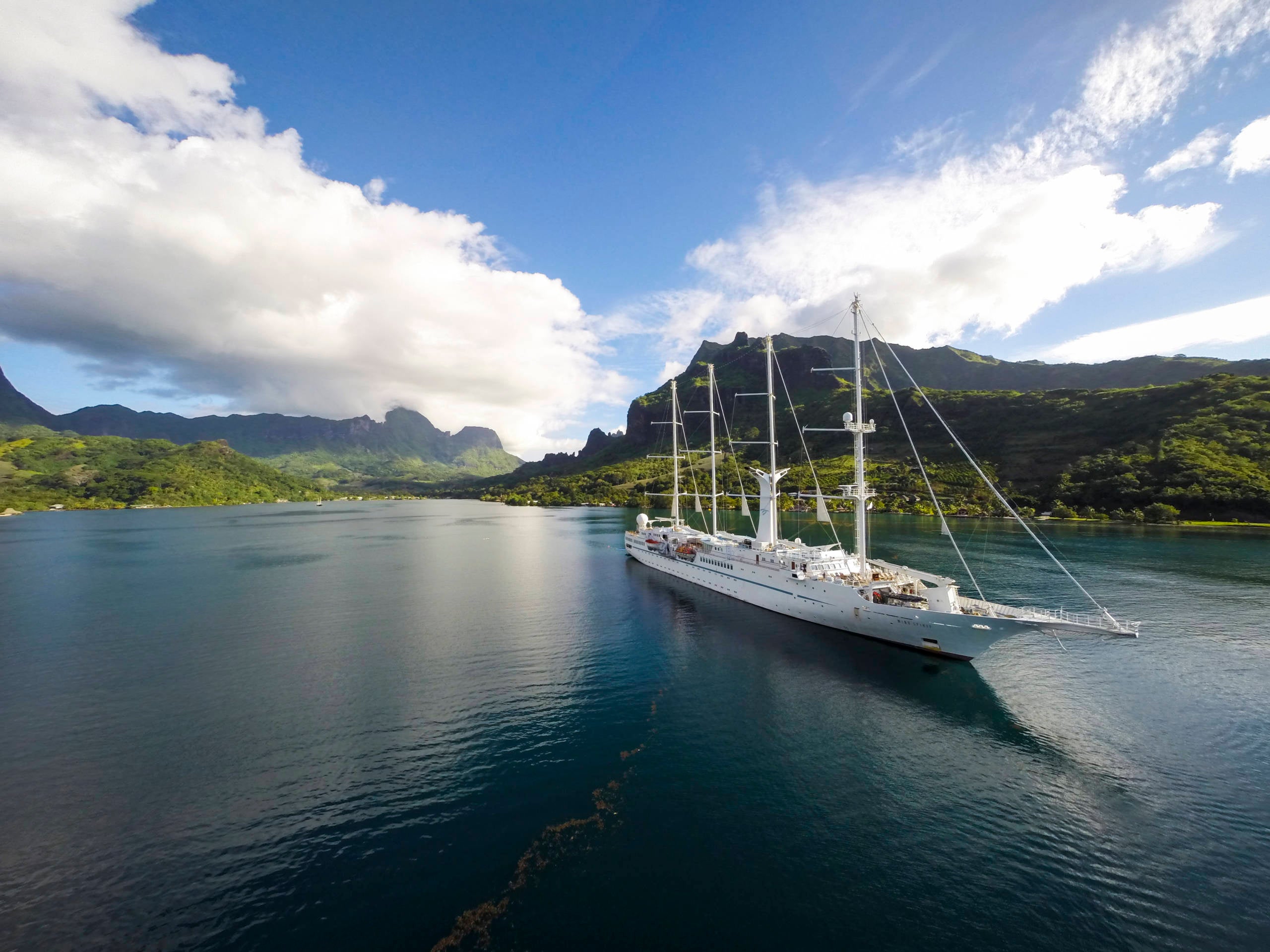 A four-masted sailing ship gliding along emerald-green water