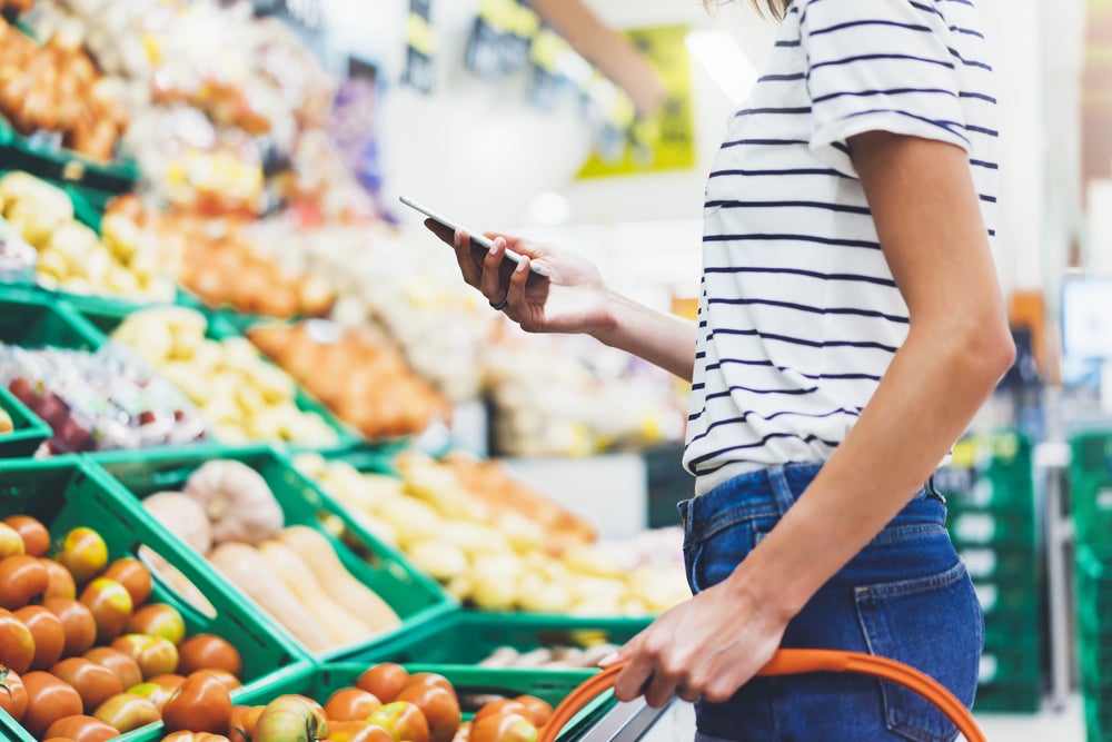 a person stands near produce in a supermarket while looking at their phone