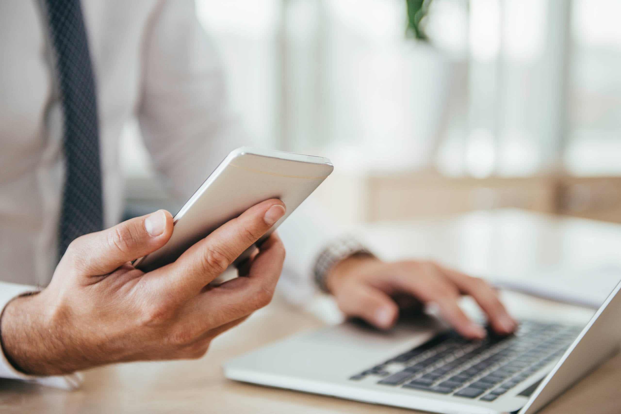 person looks at mobile phone while working on laptop