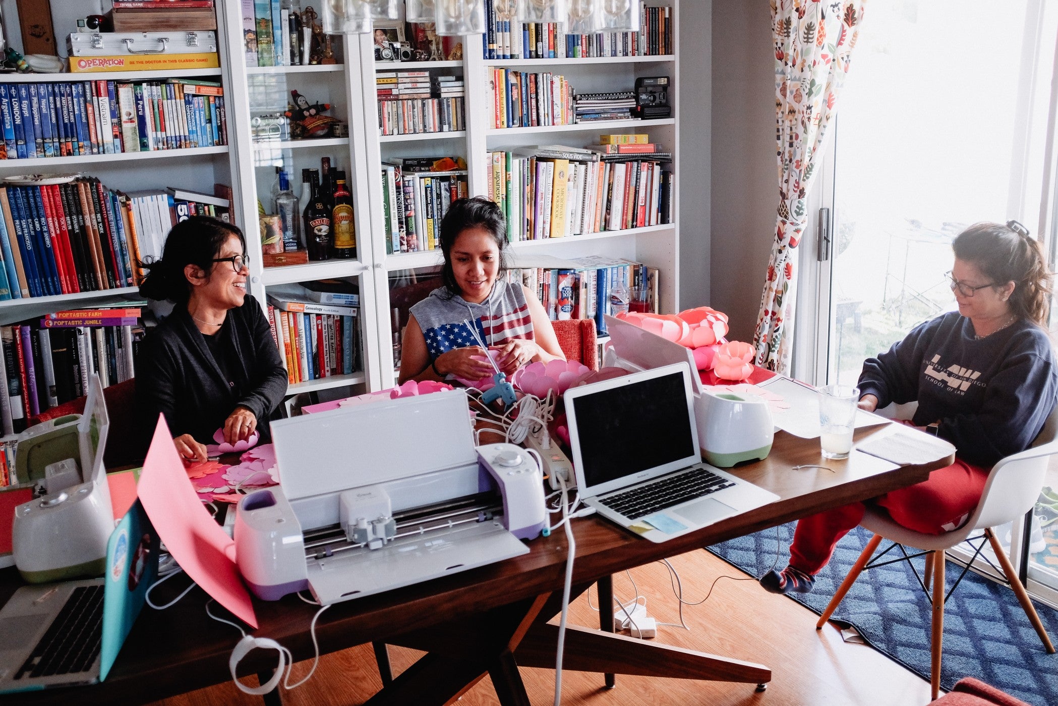 Three small-business owners sit in a home office, smiling and working. 