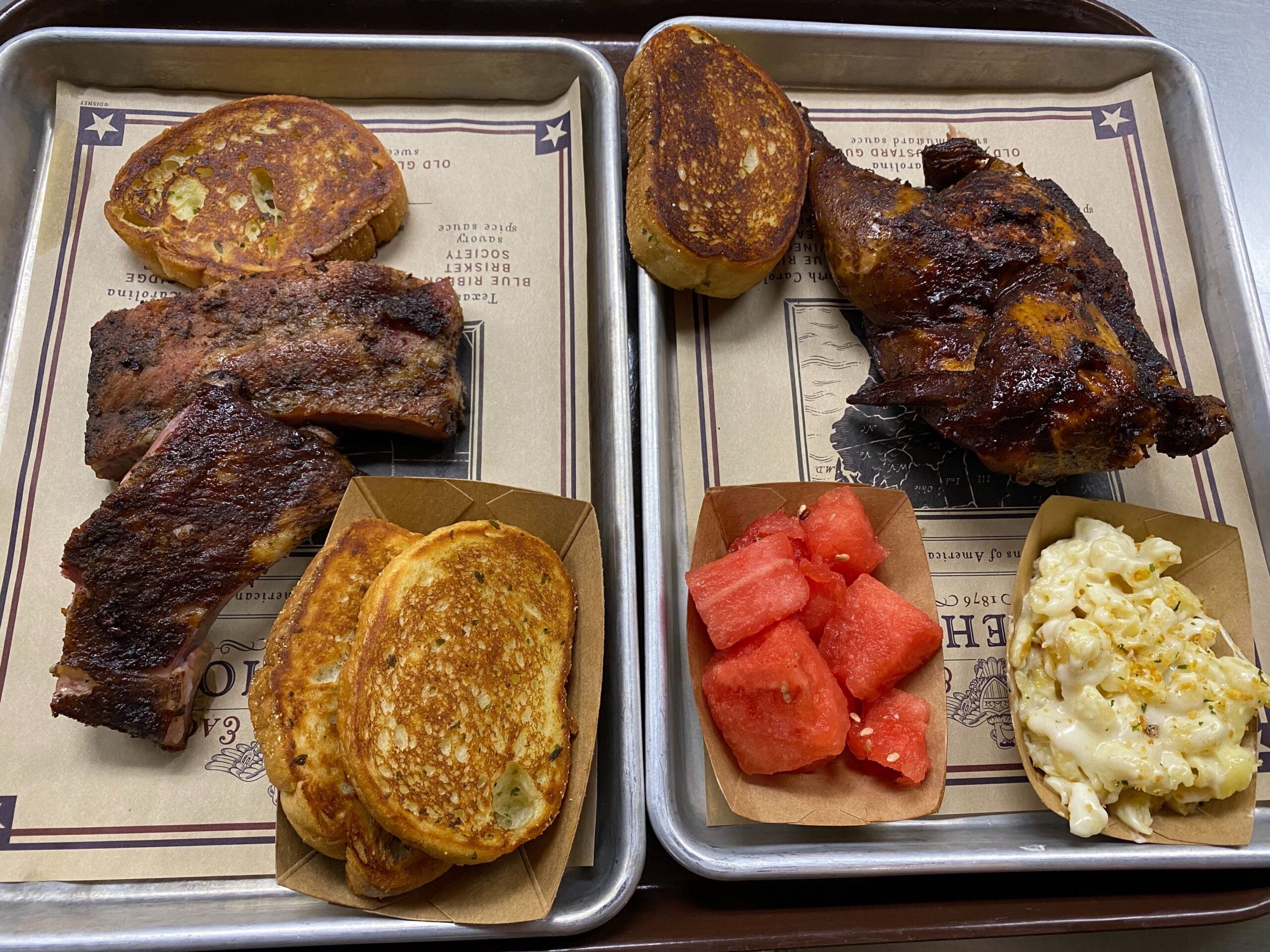 Two metal plates with barbecue chicken and ribs with toast and other side dishes at Regal Eagle Smokehouse in Epcot at Disney World