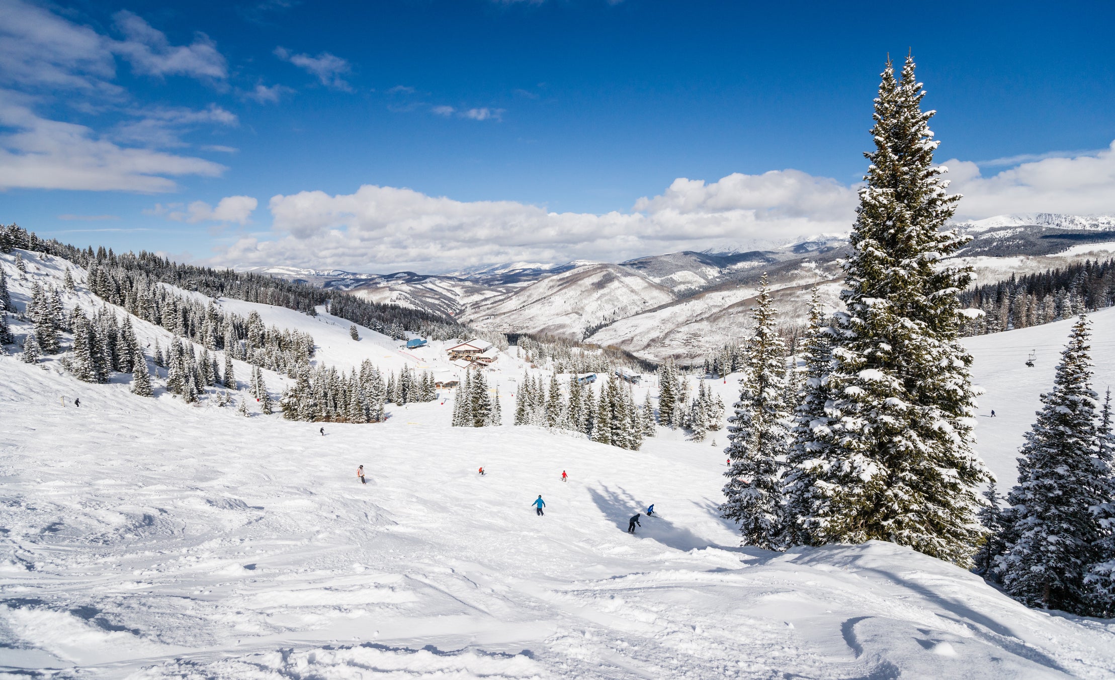 skiers dotting a snow-covered mountain under blue skies