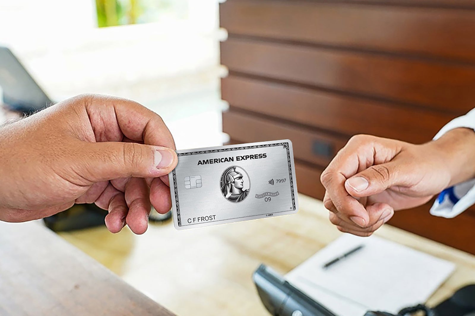 an unseen person hands the Amex Platinum Card to a cashier