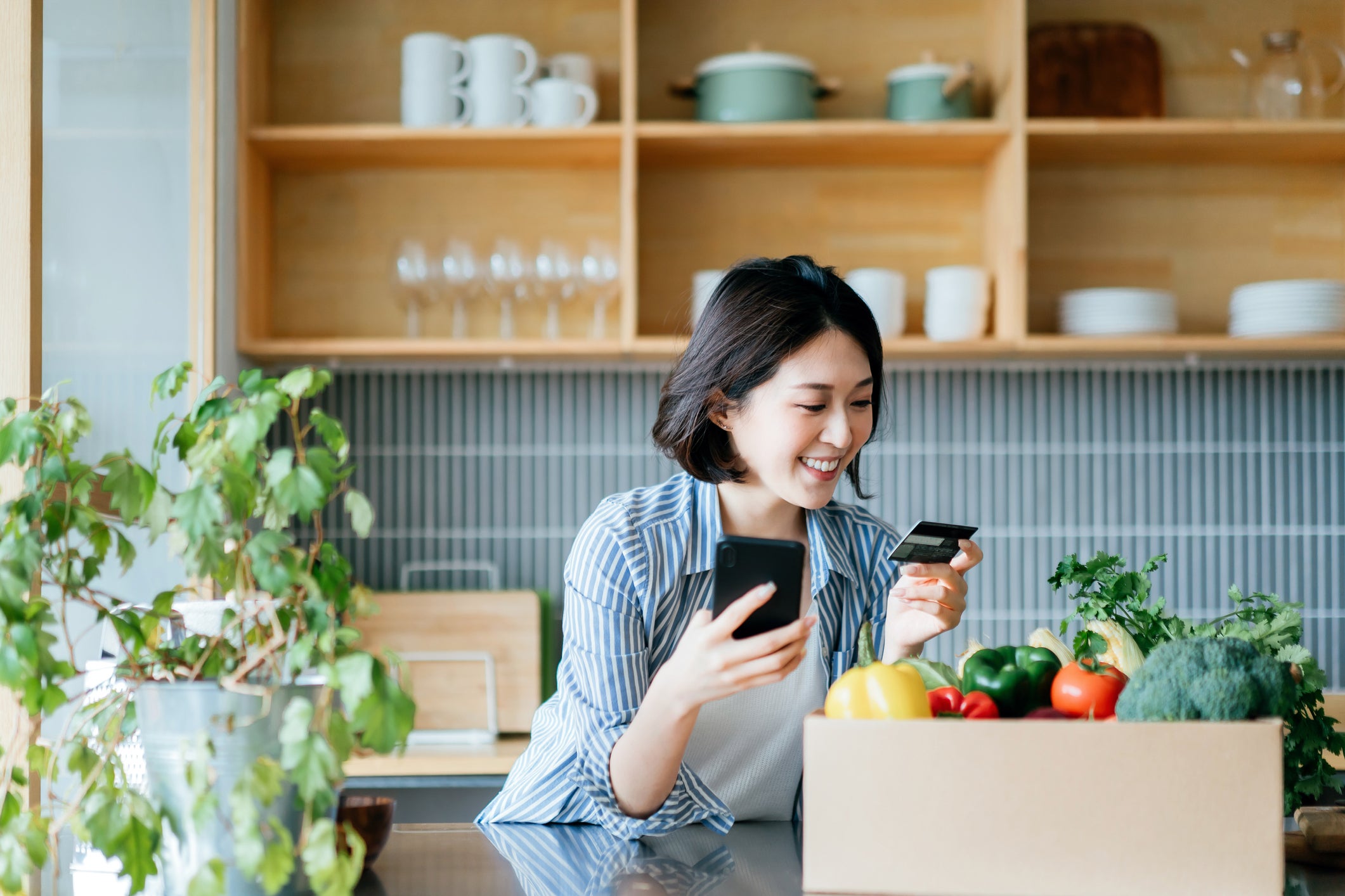 a woman in her kitchen holds a credit card while making a phone call