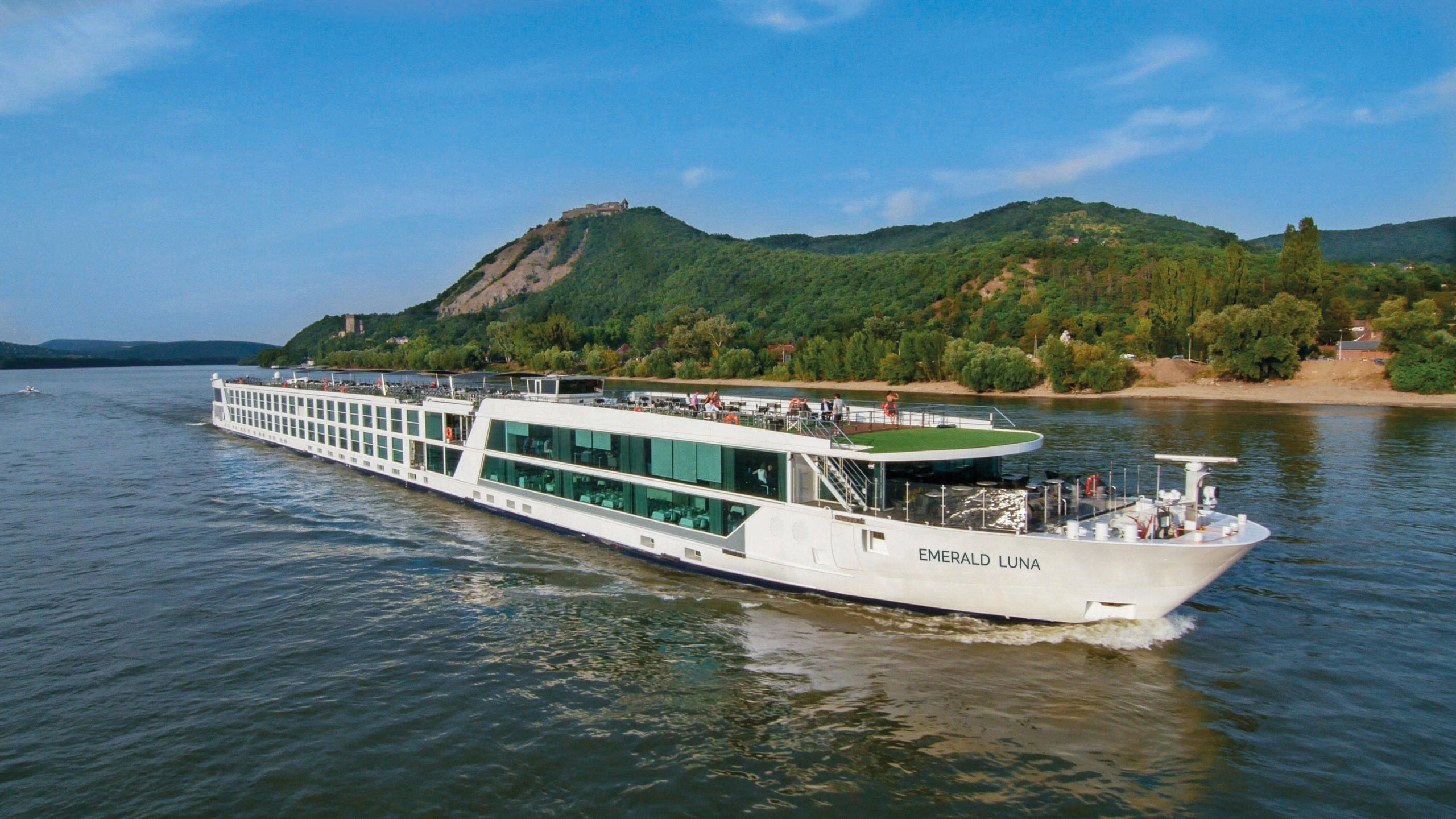 A river cruise ship sailing past a small green hill