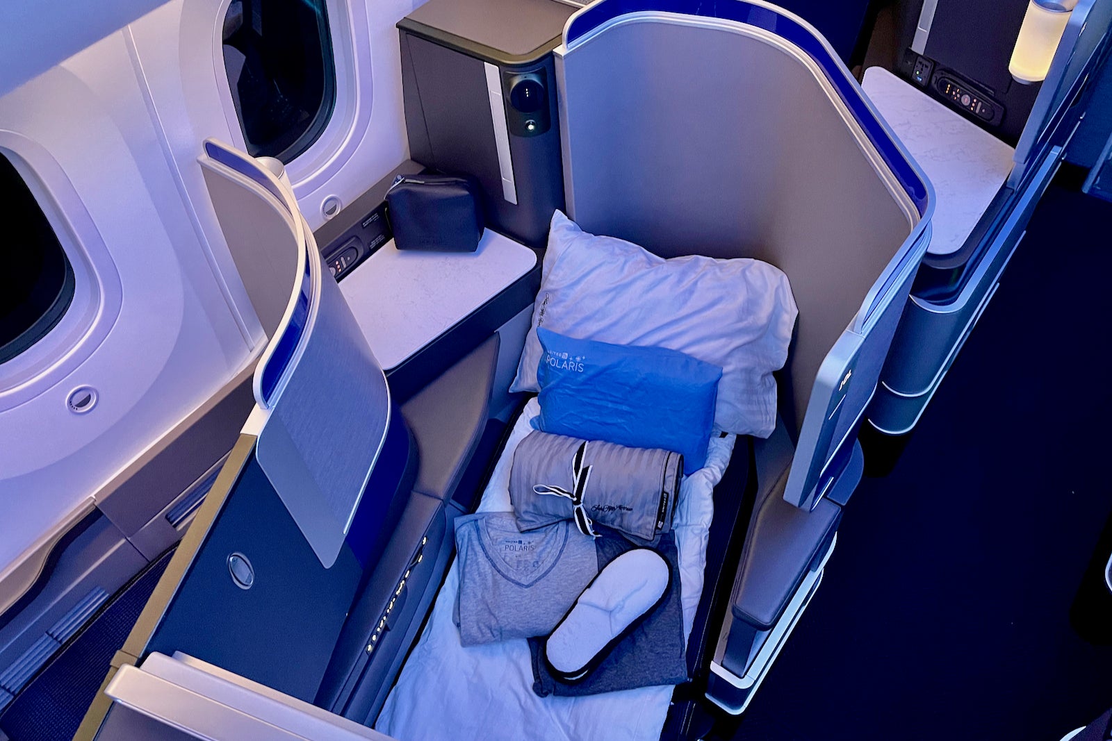 a business class seat in the lie-flat position with amenities on top of the bedding