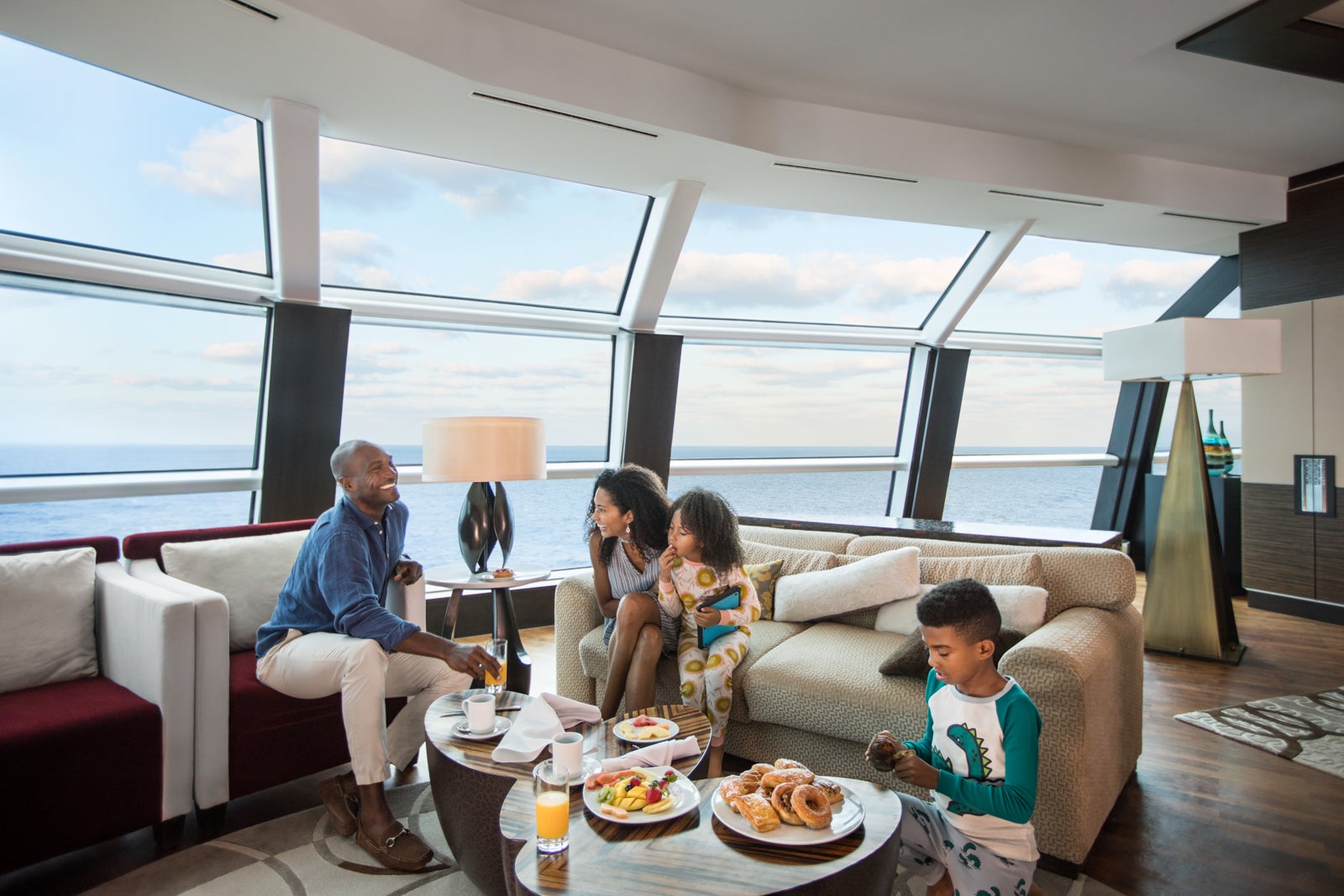 A family of four sits in the living room of a cruise ship suite eating room service breakfast