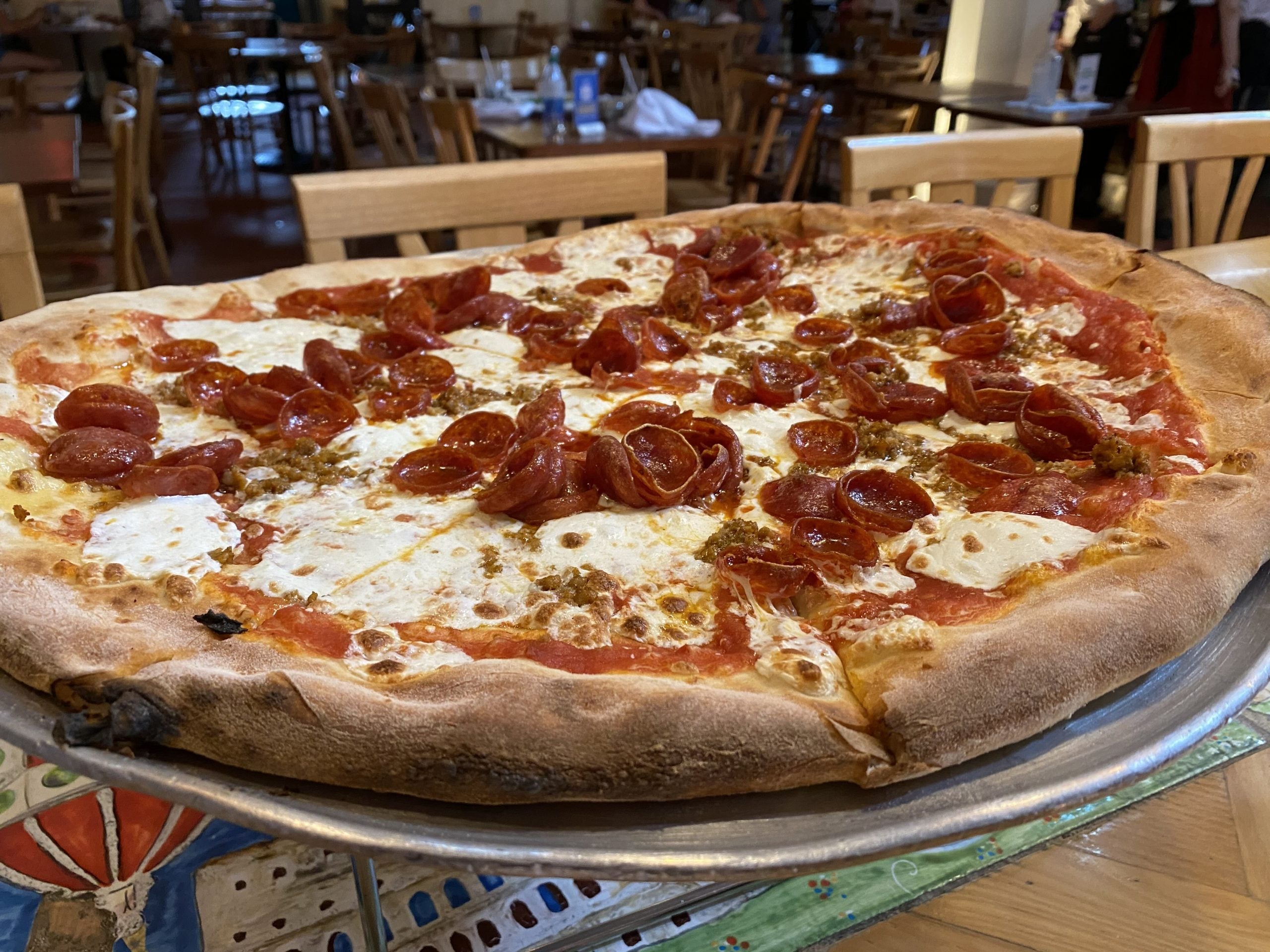 A large pizza with sausage is served on an aluminum pan at the Via Napoli restaurant at Epcot in Disney World