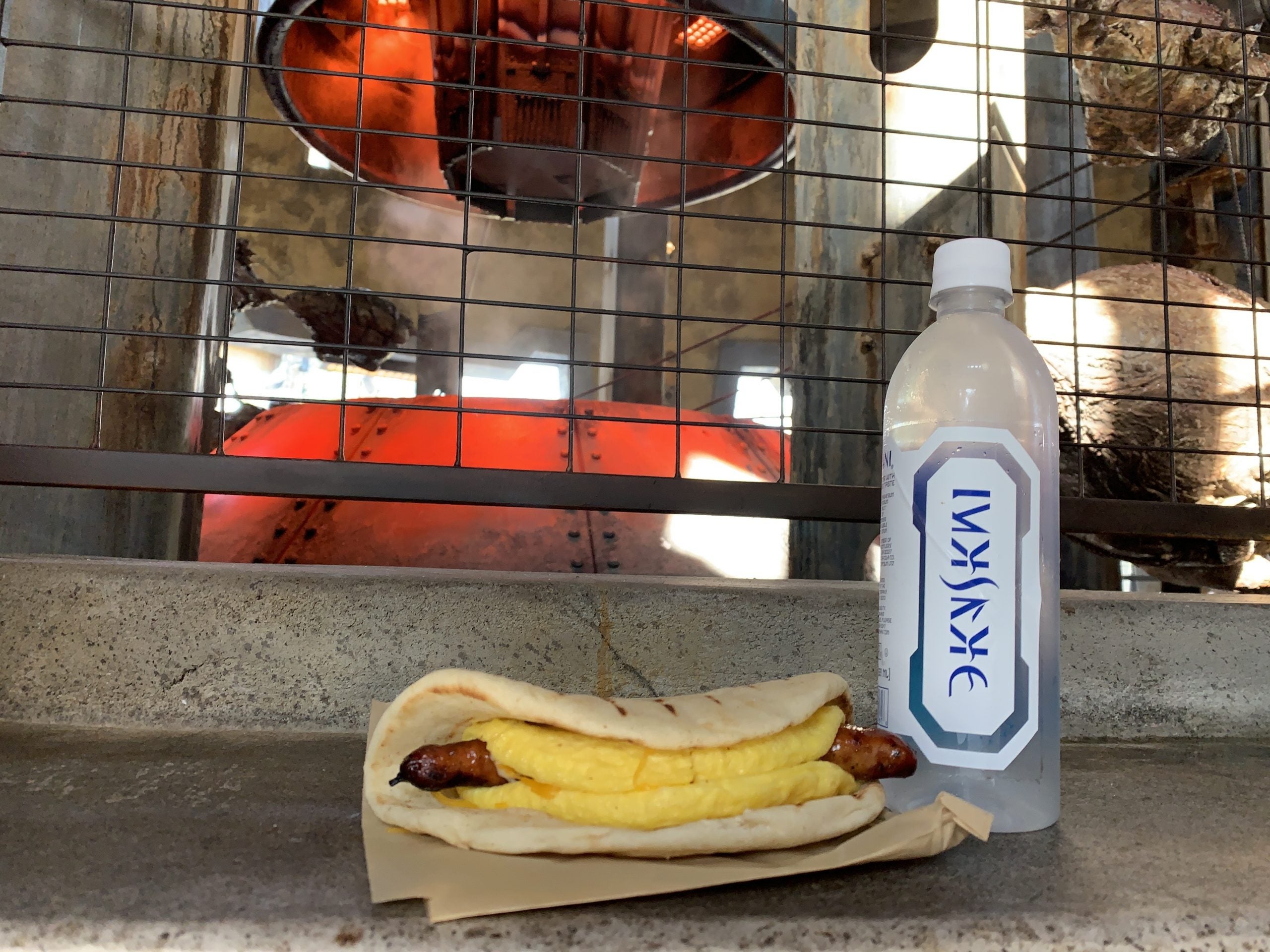 A breakfast Ronto Roaster with sausage and eggs in a pita sits on a shelf next to a bottle of water at Ronto Roasters in Star Wars: Galaxy's Edge at Disney World