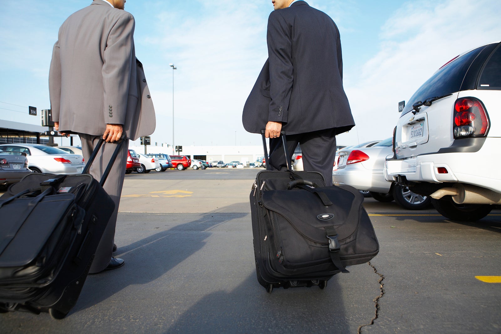 two men in suits with suitcases in car lot