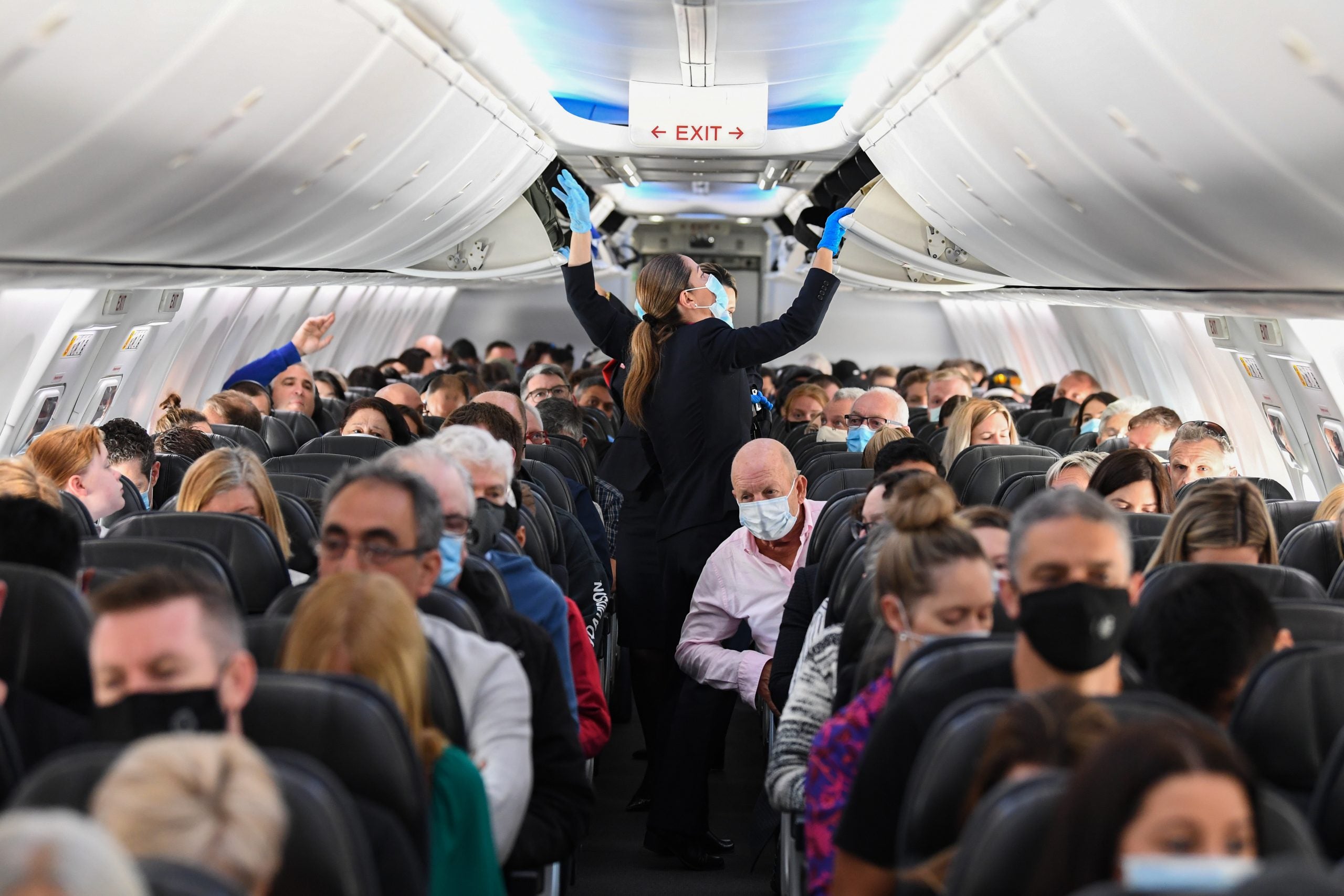 a flight attendant closes overhead bins while a plane full of passengers wait in their seats