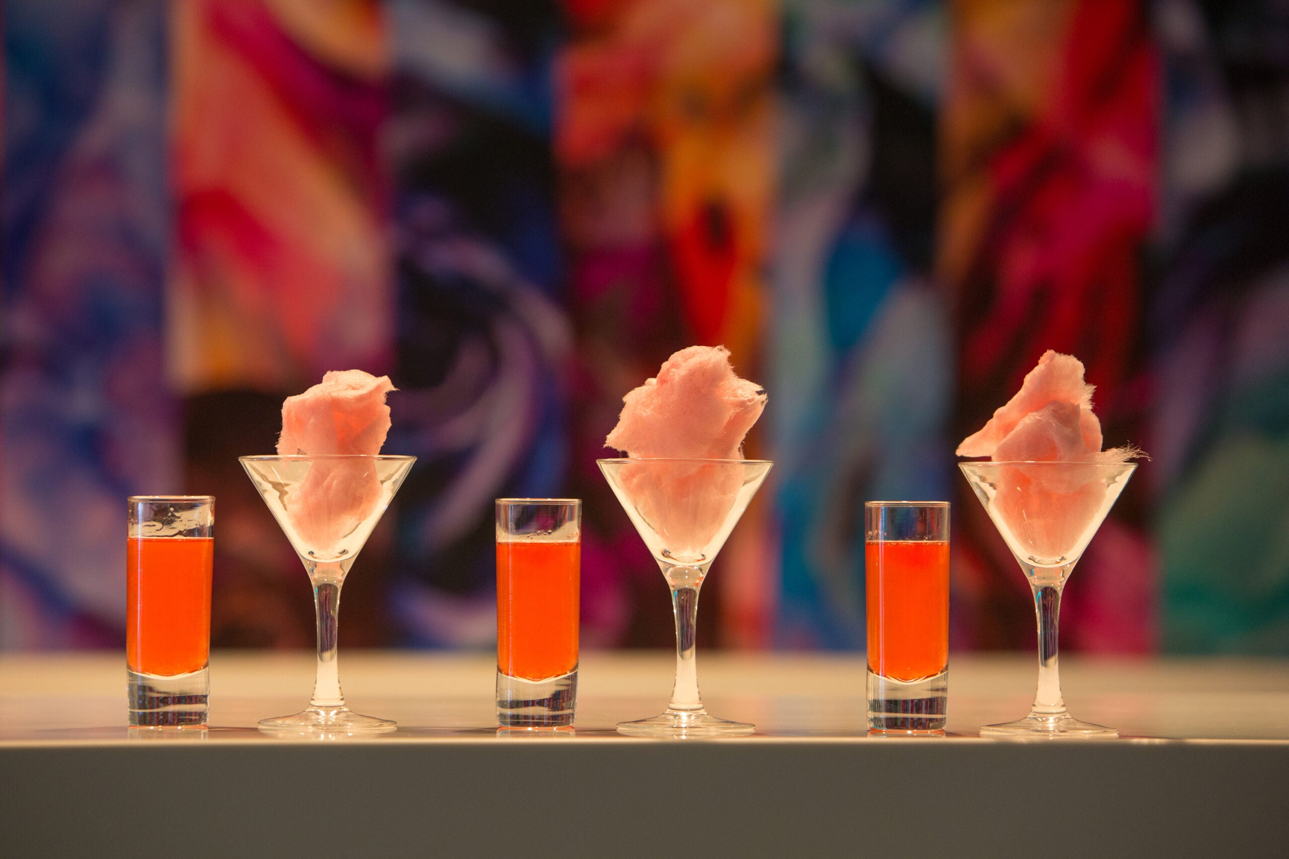 Three shot glasses of orange liquid with three martini glasses of pink cotton candy