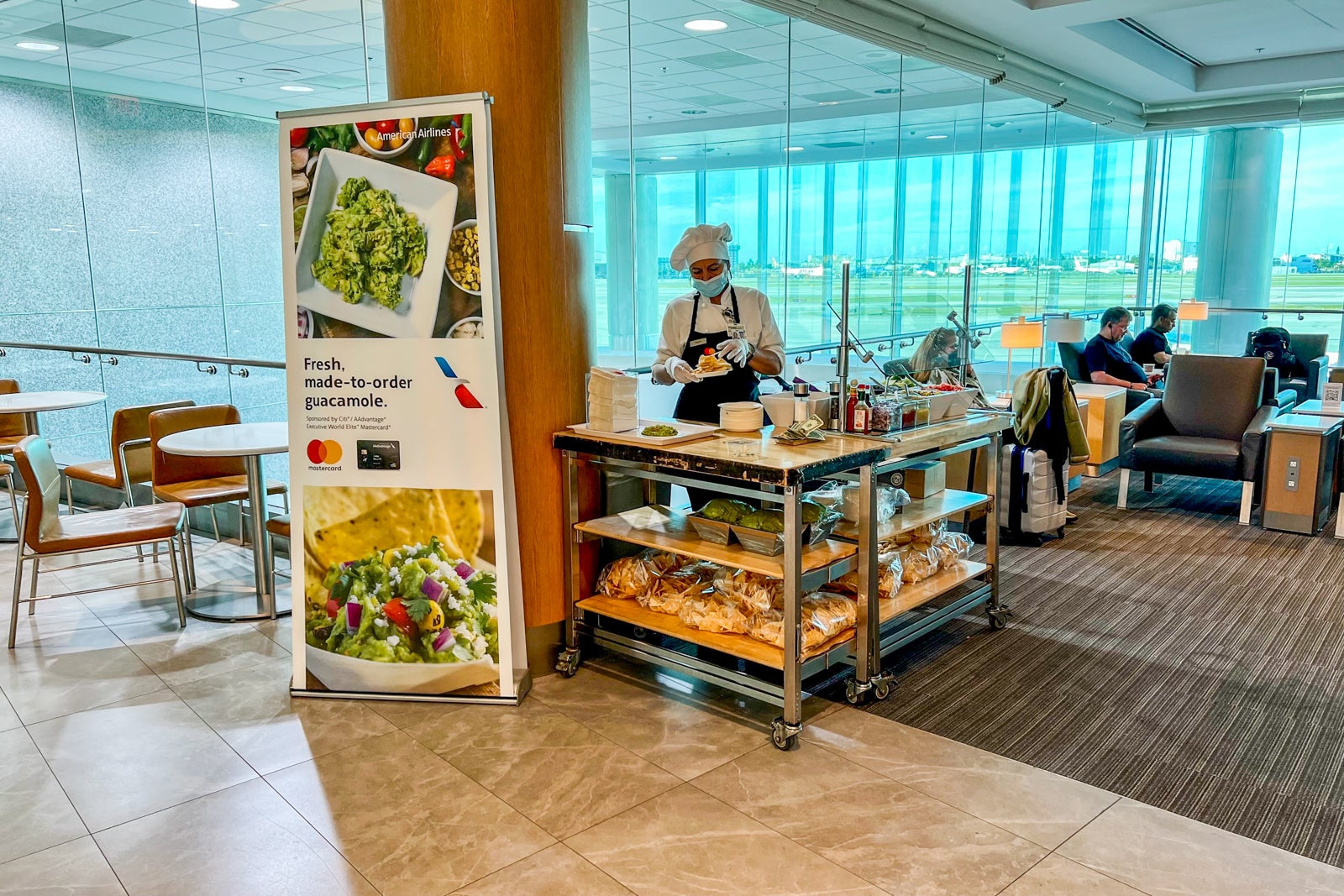 an employee is next to a sign at the made-to-order guacamole stand in an airport lounge