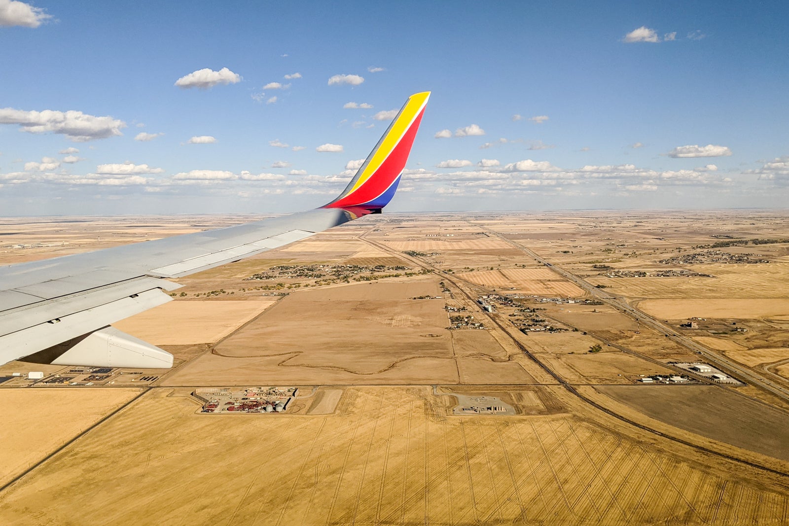 A view looking out the window of a Southwest Airlines plane, with a blue sky, clouds and brown fields