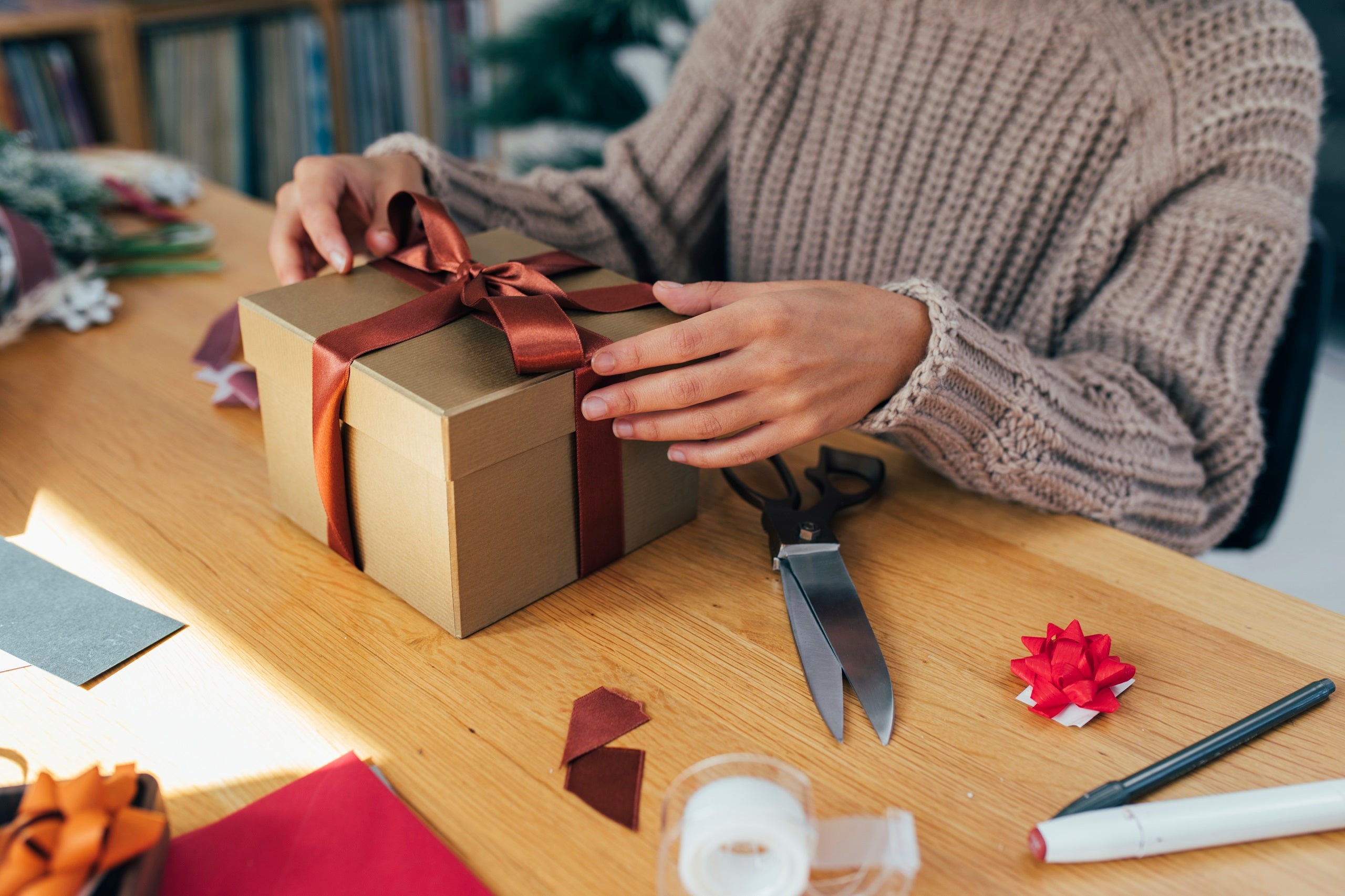 A person wraps a gift box with a bow on top