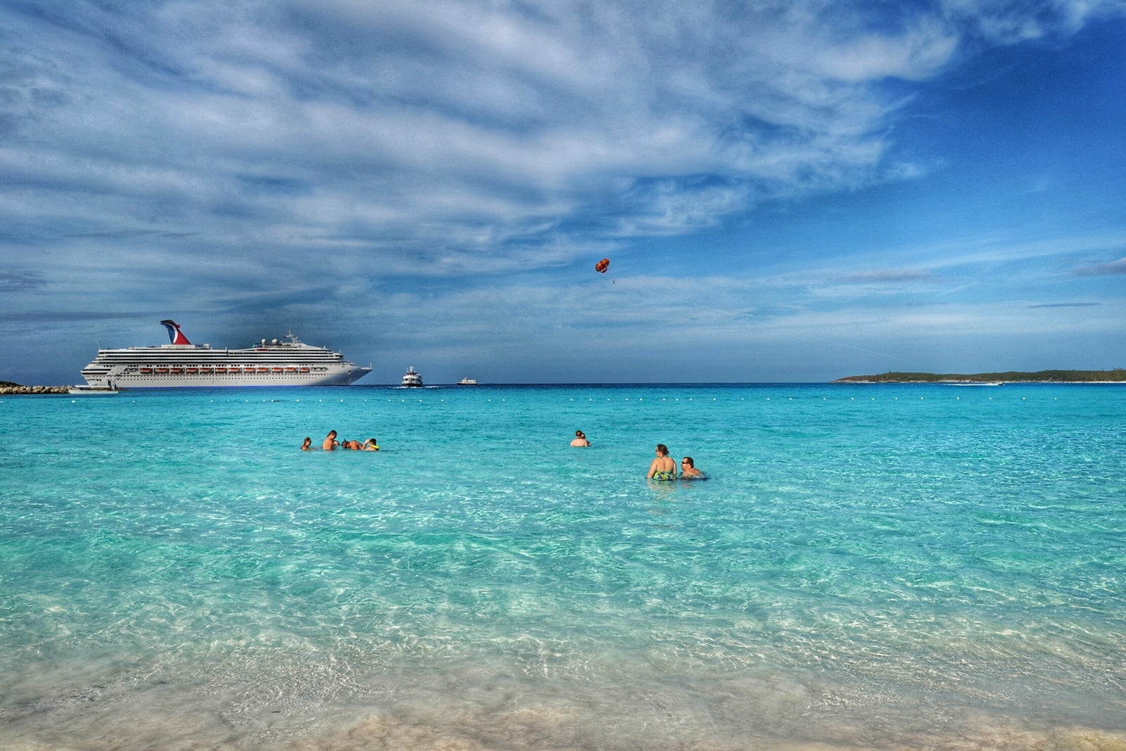Cruisers in clear, turquoise water near the beach with a cruise ship anchored in the distance