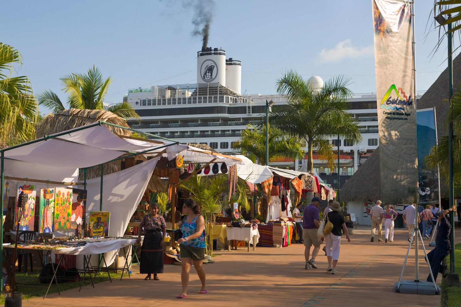 An open-air market with a cruise ship docked in the background