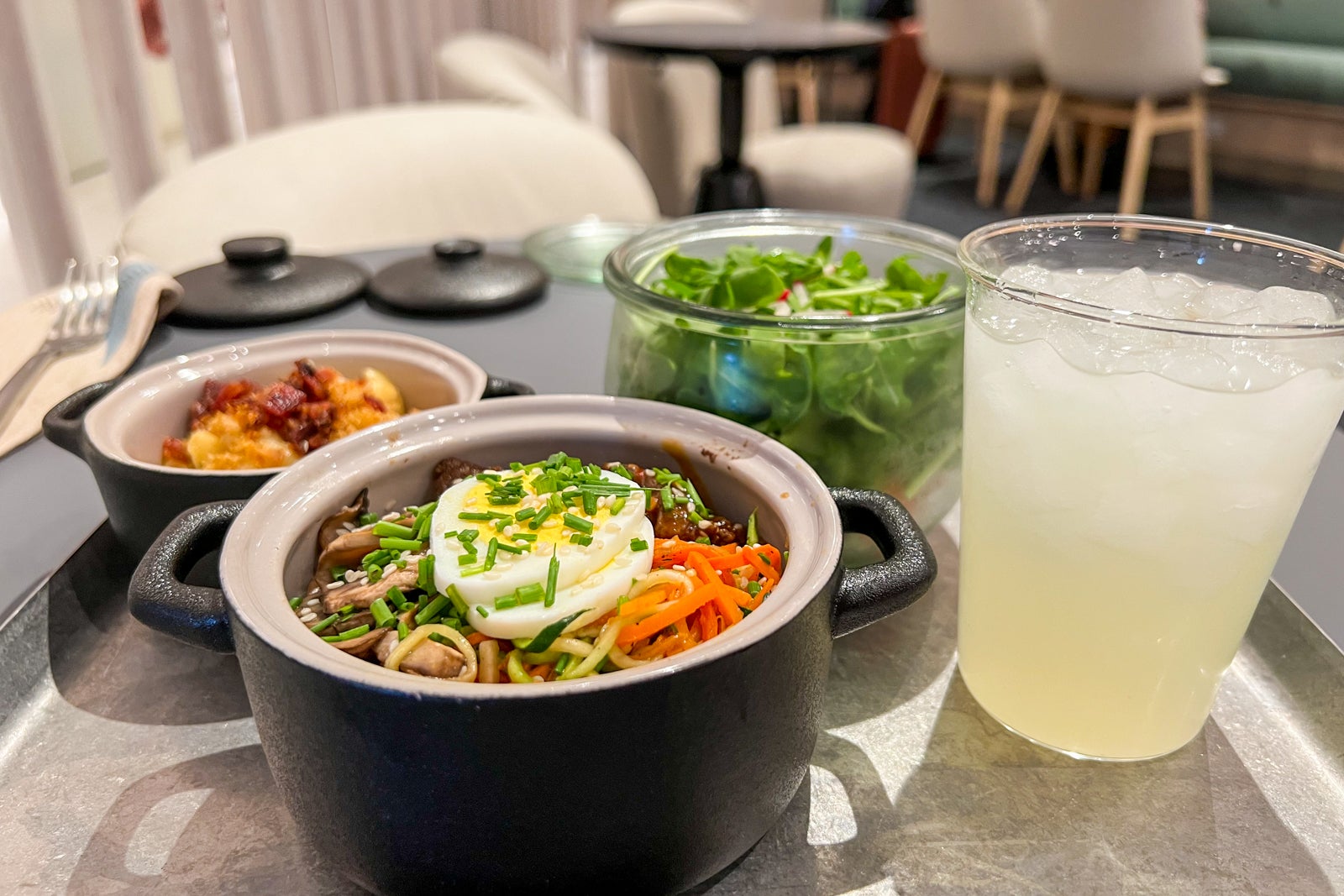 a tray with various food bowls and a glass of lemonade