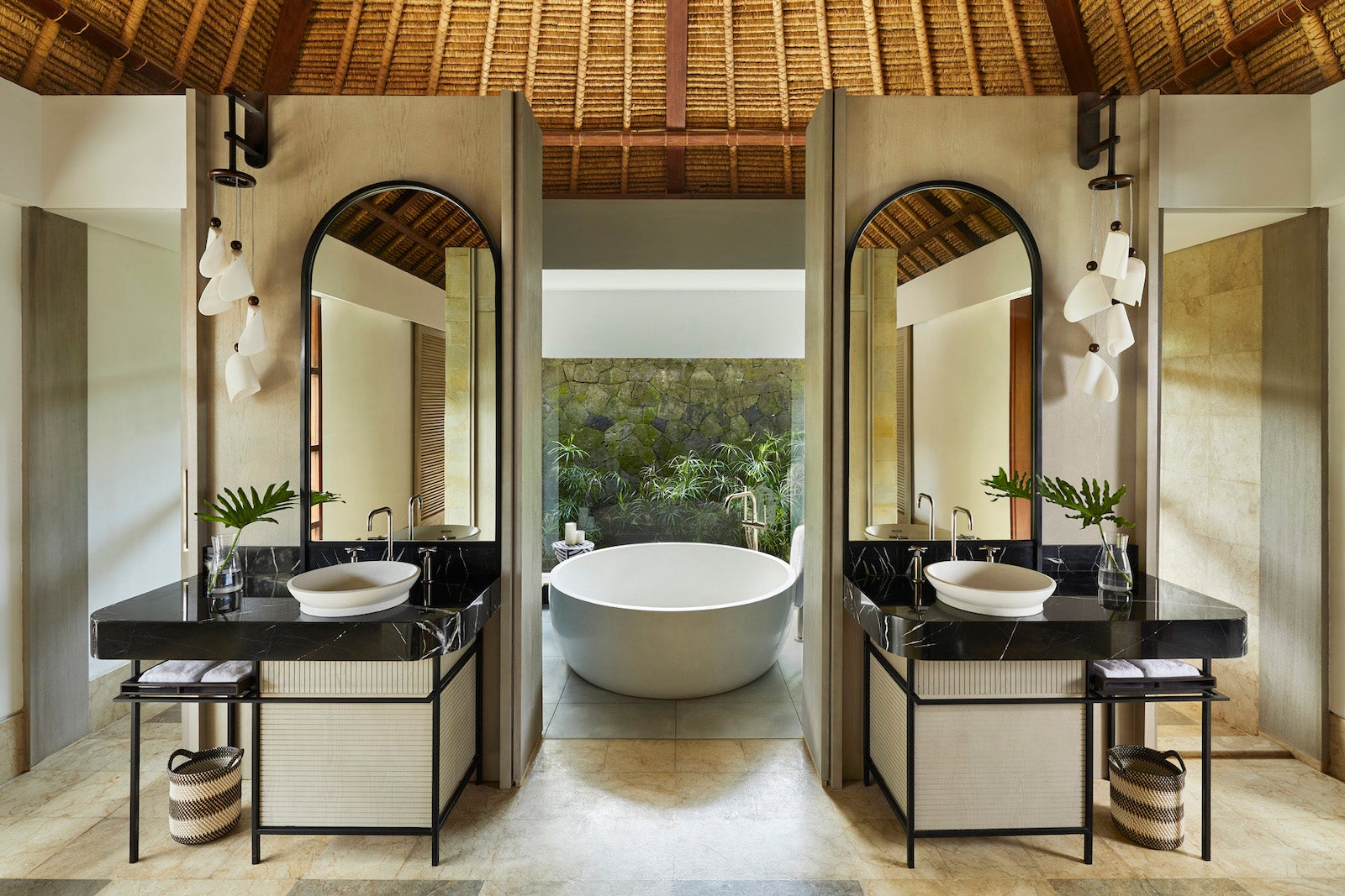 large indoor-outdoor bathroom with two sinks and large mirrors and a large round bathtub looking outside