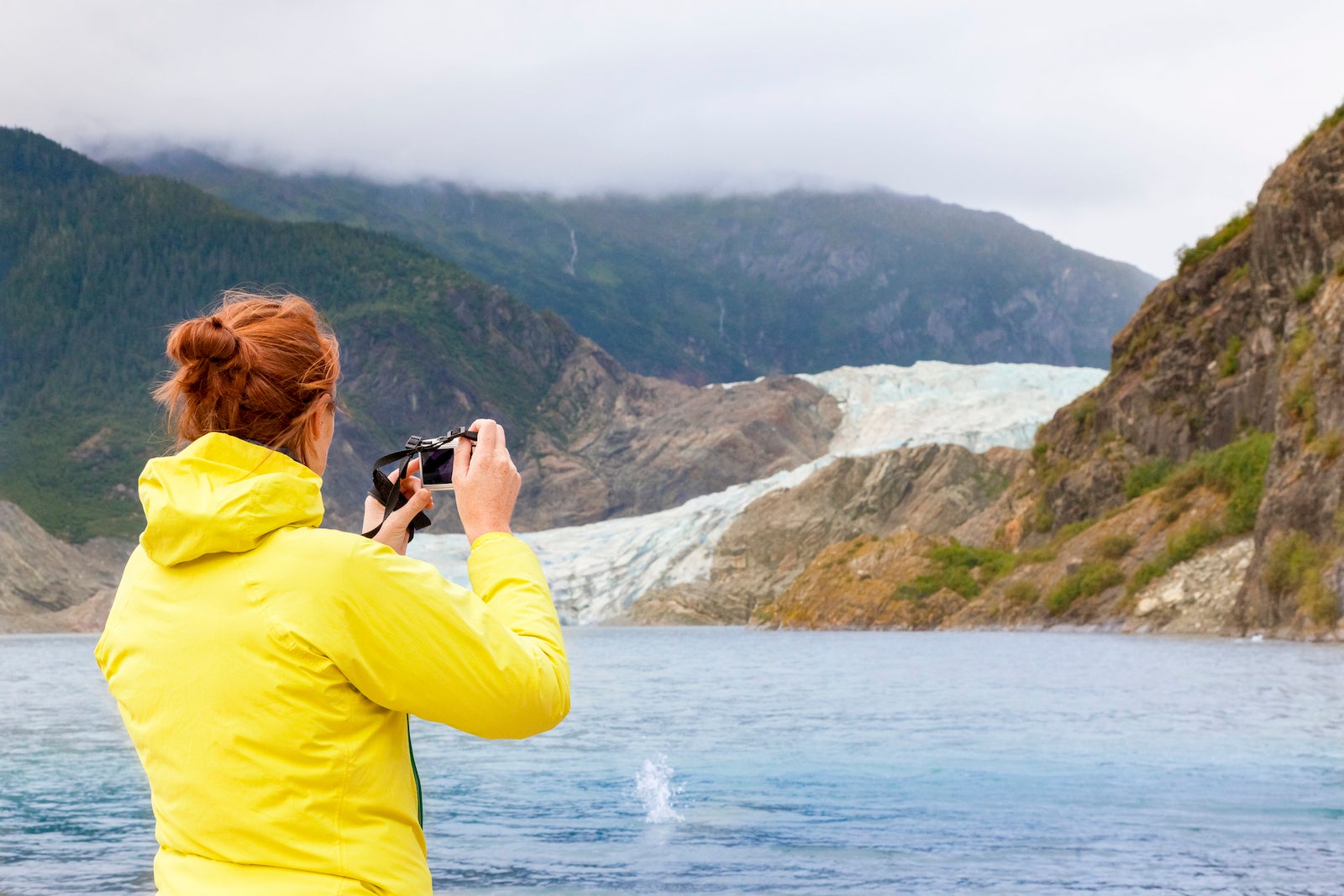 Woman in yellow rain jacket taking photo of glacier in Alaska