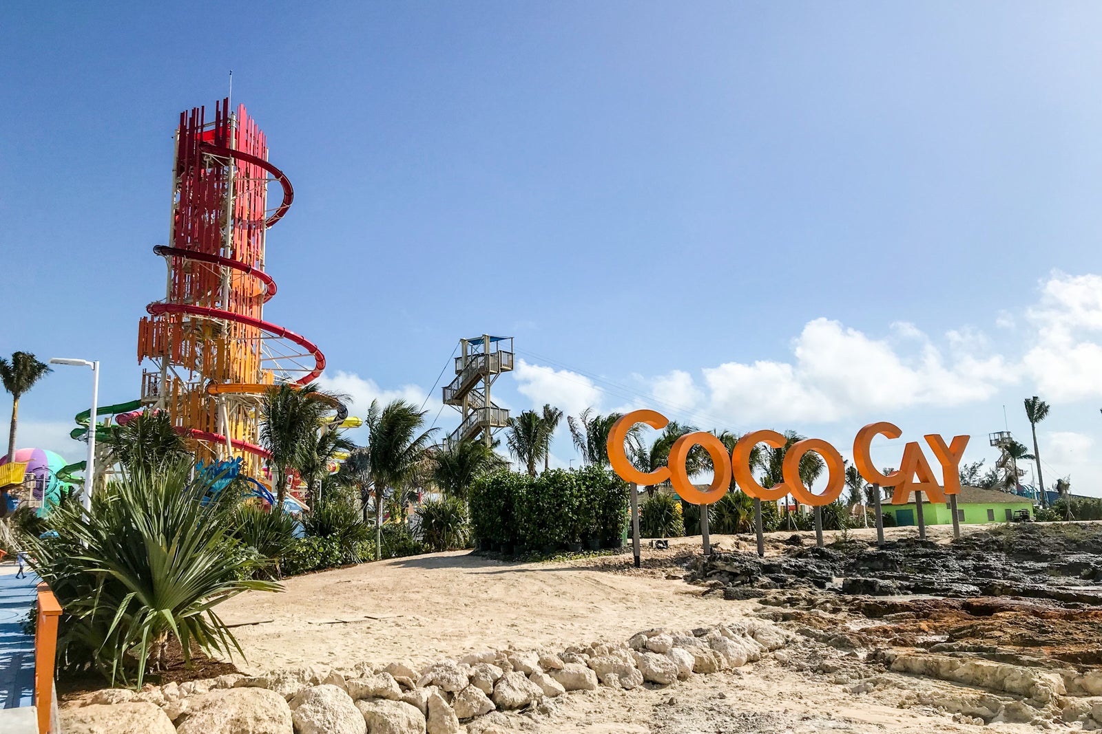 A large spiral waterslide rises up into blue sky on an island with a large orange sign reading 