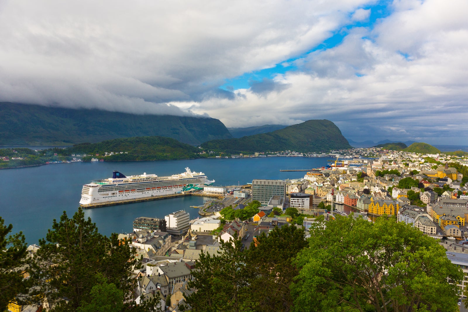 A cruise ship anchored in port with a town in the foreground and a mountain in the background