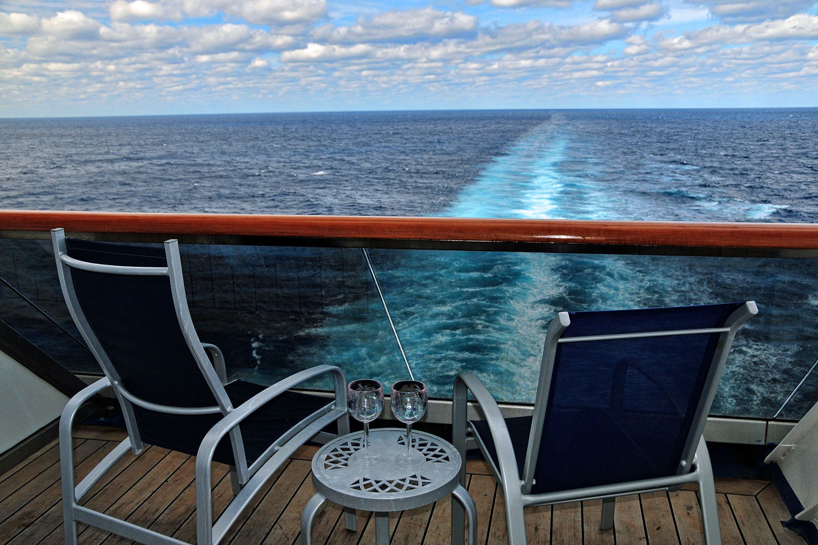 Two empty chairs on the back balcony of a cruise ship overlook the trailing wake of the ship