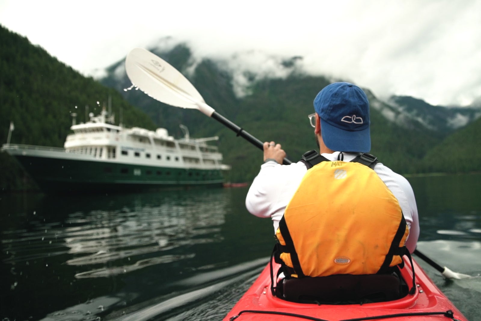 Lone kayaker in Alaska with expedition ship and mountains in the background