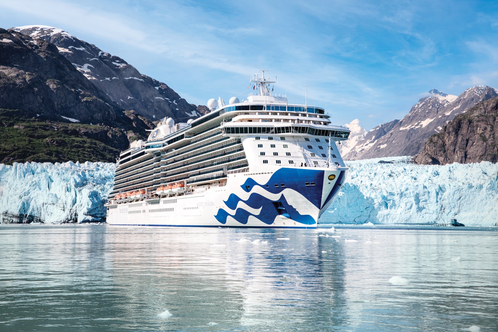 A white Princess cruise ship with a blue sea witch painted on the hull anchored in front of a blue glacier in Alaska