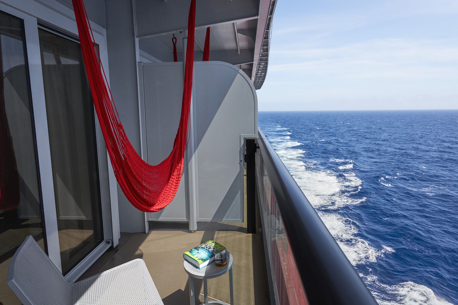 Cruise ship balcony cabin with red hammock swing, chair and table