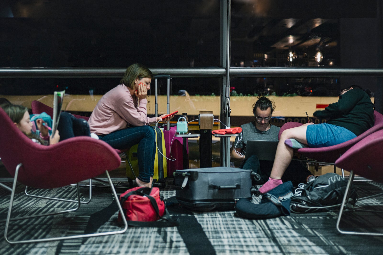 group of travelers sitting in chairs and on floor looking at their phones